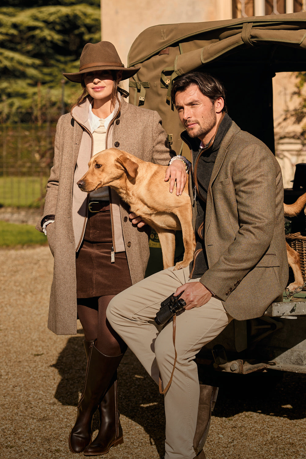 Man and woman with a dog standing next to a vintage car in an outdoor setting