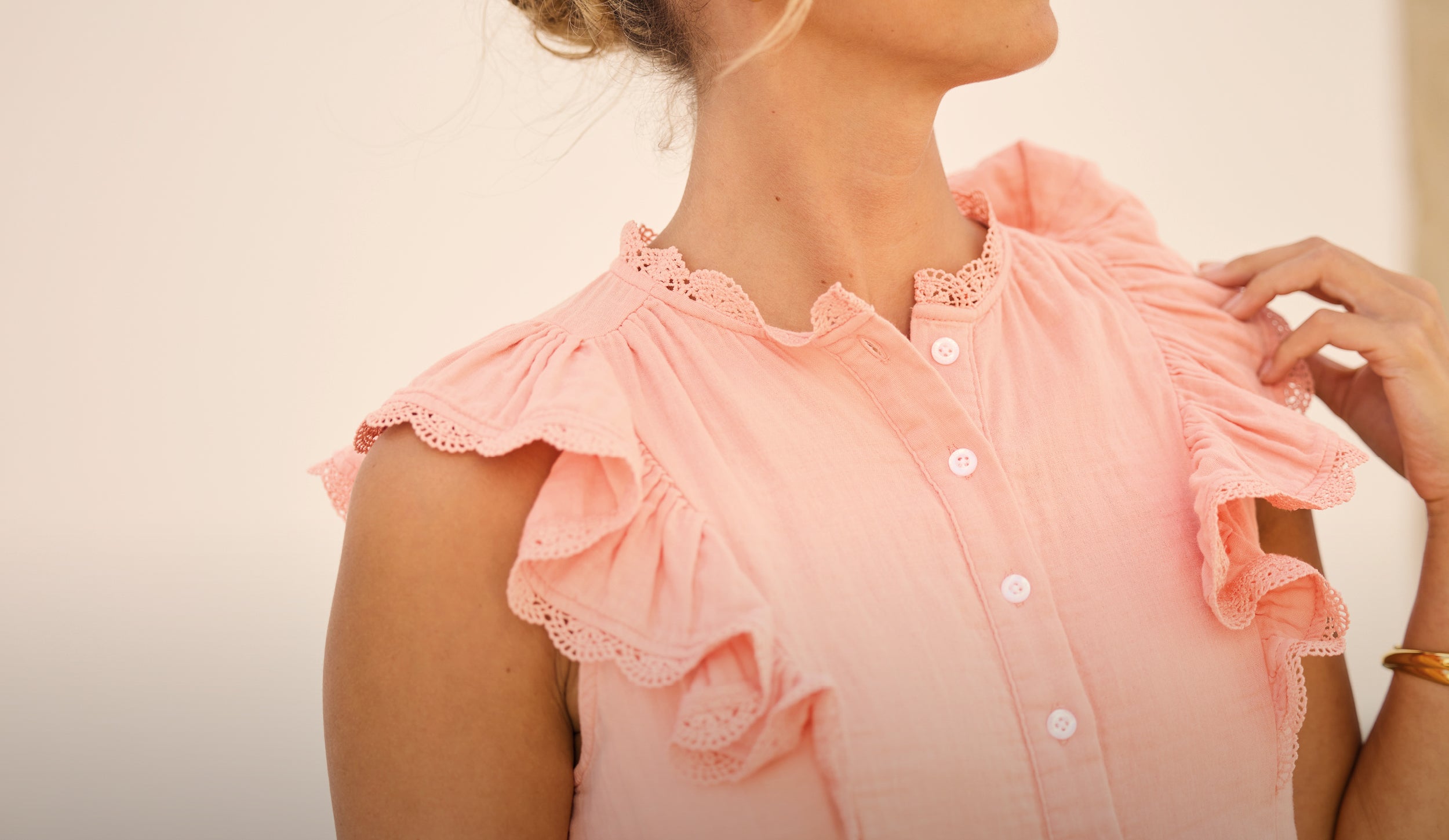 Woman wearing a light pink blouse with ruffled sleeves against a neutral background