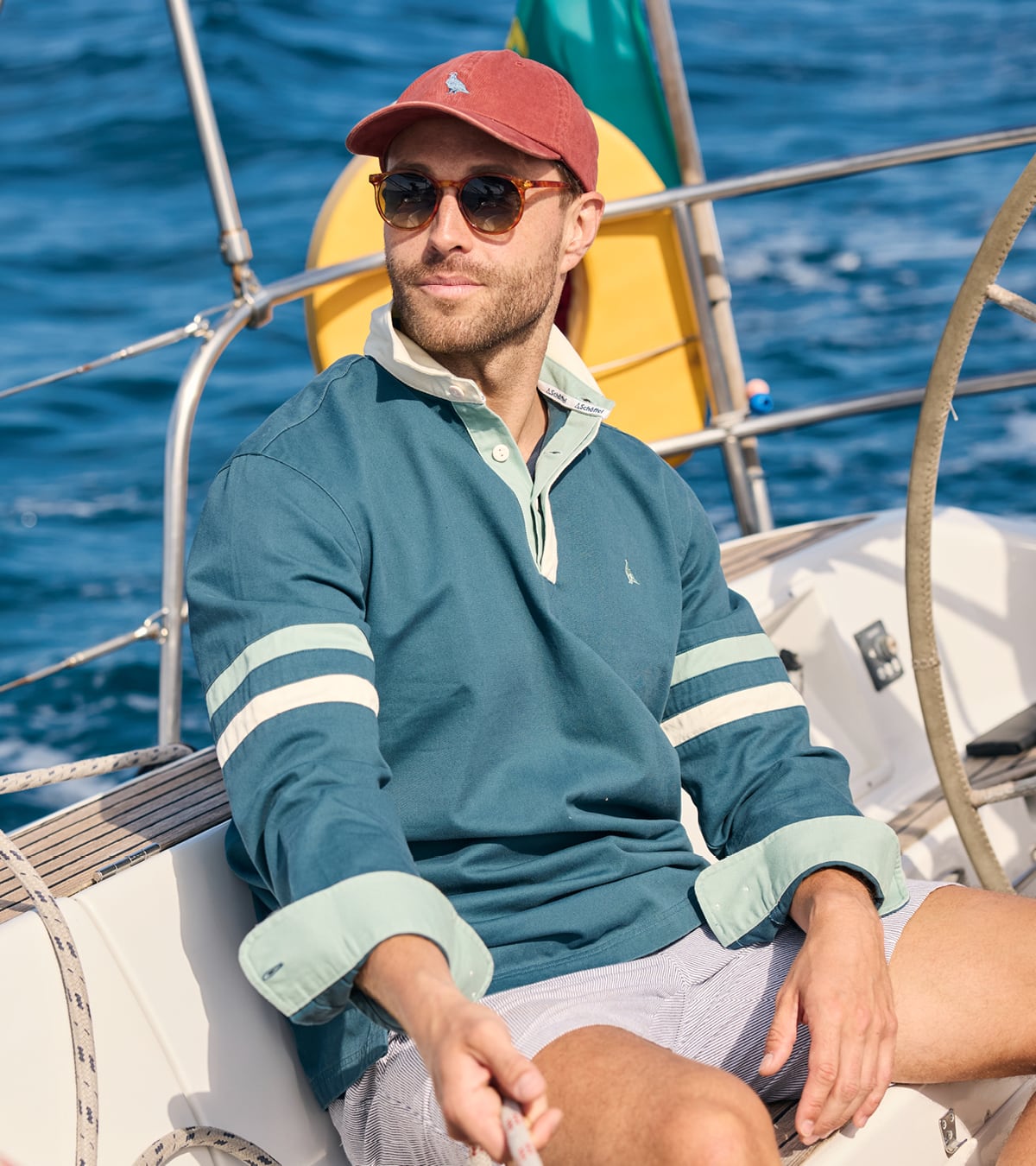 Man on a sailboat wearing a teal sweater with white stripes and sunglasses.