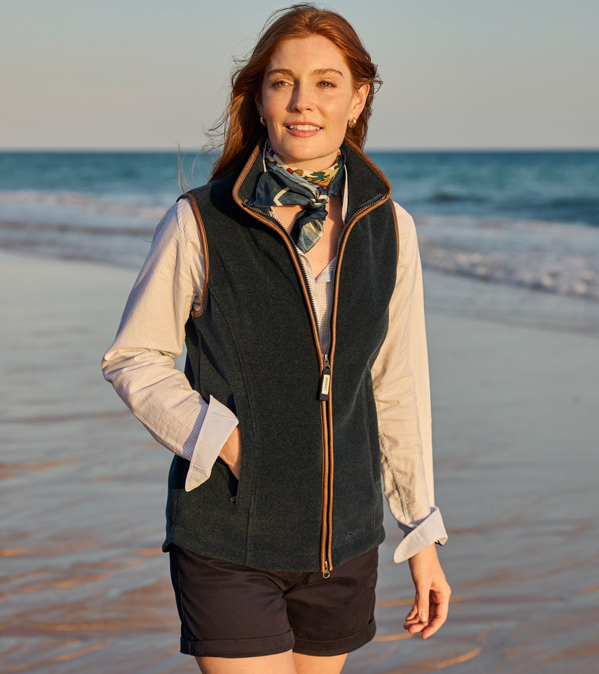 Woman standing on a beach wearing a navy blue Schoffel gilet and silk scarf