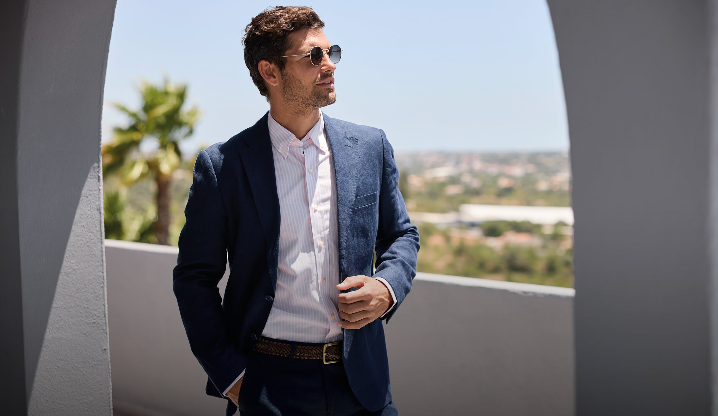Man in a linen blue suit standing on a balcony with a scenic view