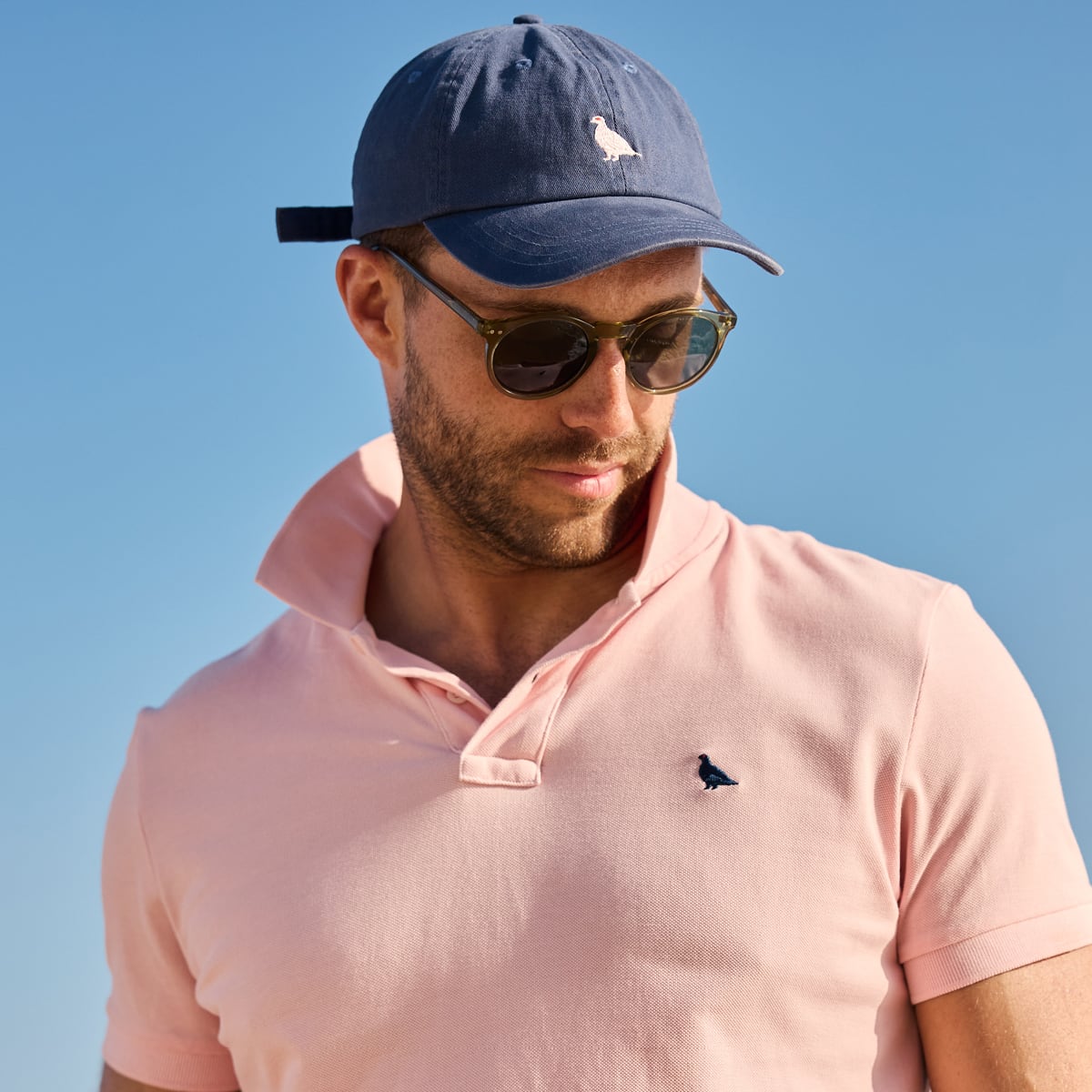 Man wearing a pink polo shirt and navy cap with a clear blue sky background