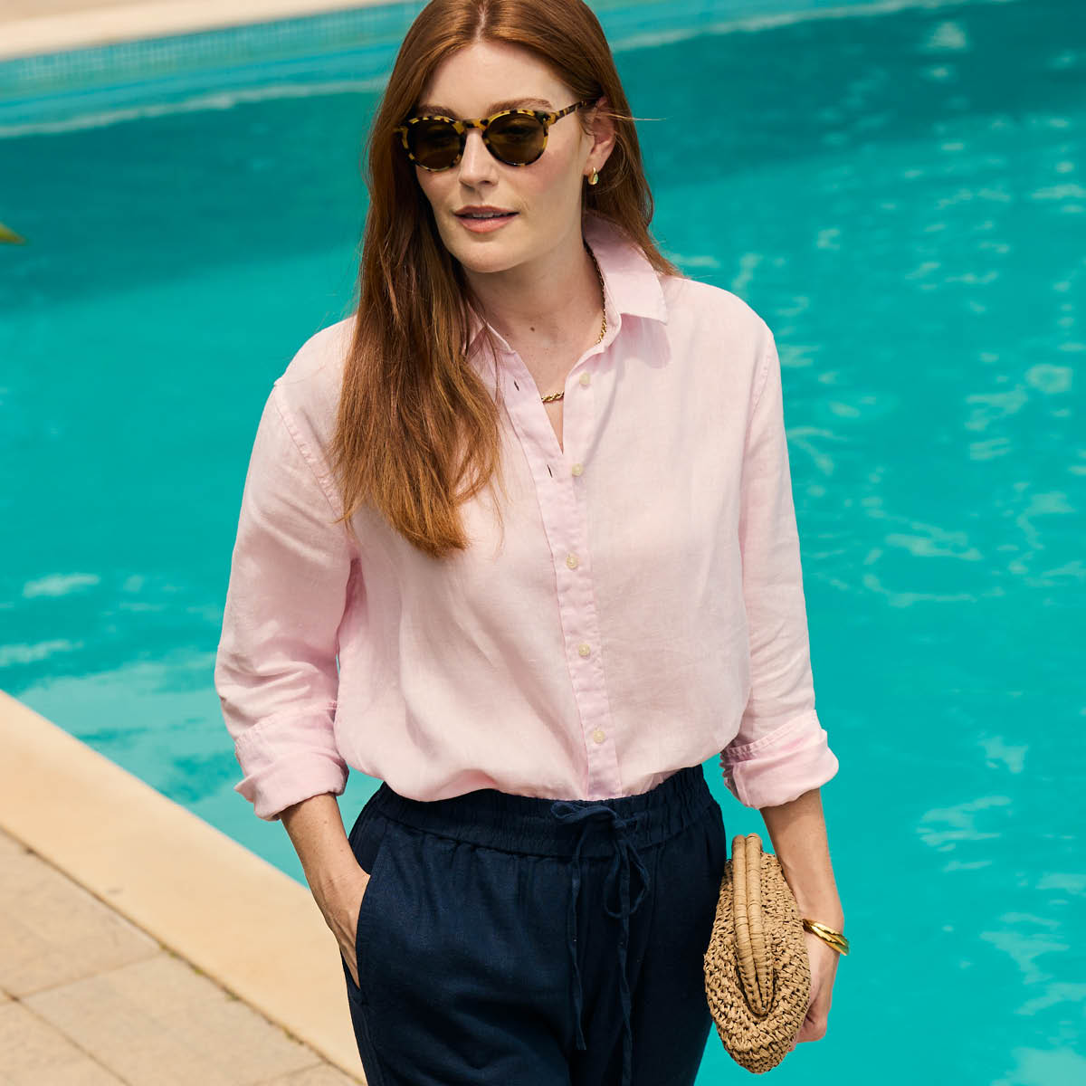 Woman in a pink shirt and navy trousers standing by a pool