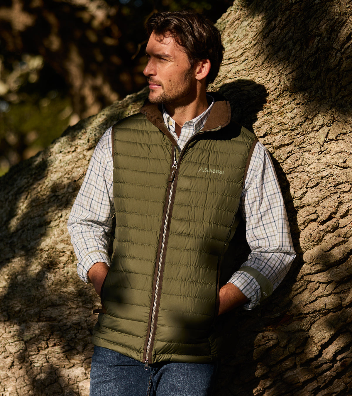 Man wearing a green puffer vest leaning against a textured wall.