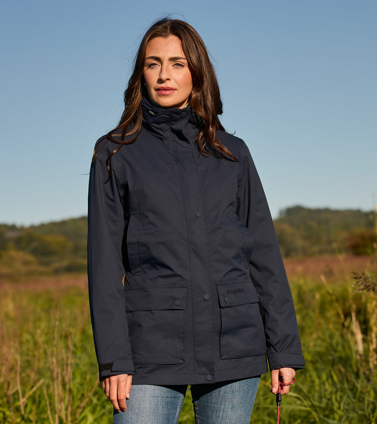 Woman wearing a navy blue jacket standing in a field with a clear sky.