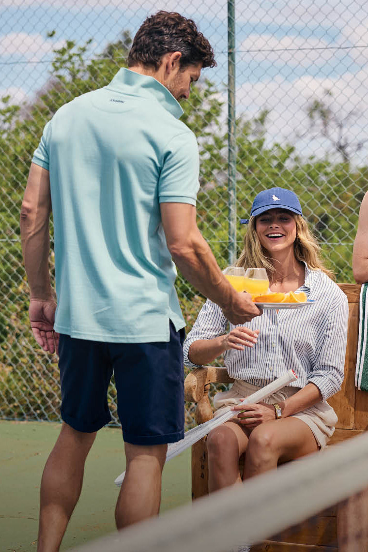 Man in light blue shirt and navy shorts shaking hands with a woman on a tennis court.