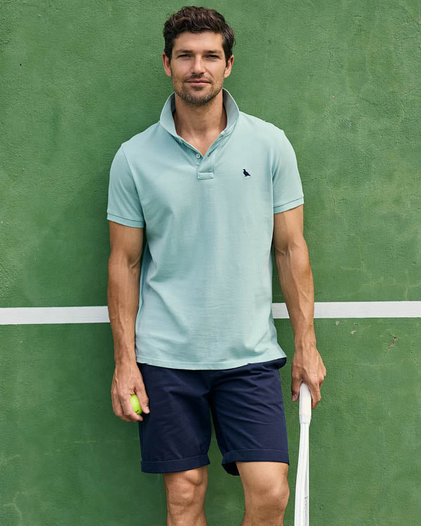 Man holding a tennis ball and racket on a green tennis court