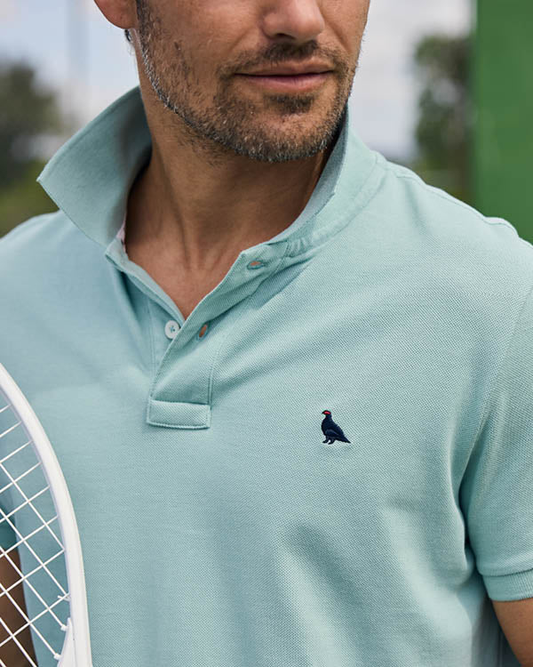 Man wearing a light blue polo shirt with a logo, holding a tennis racket.