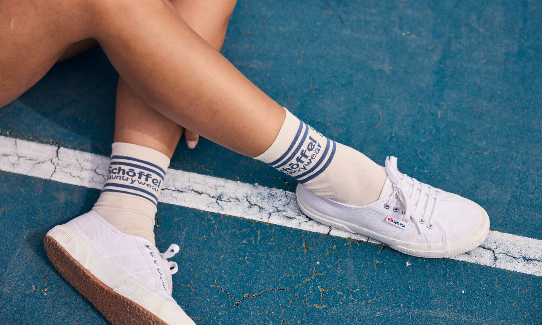 Person wearing white trainers and socks with visible branding on a blue surface