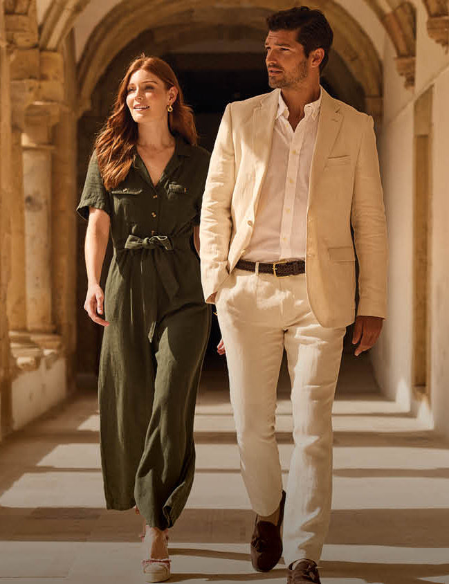 Man and woman walking together in a sunlit hallway with stone arches.
