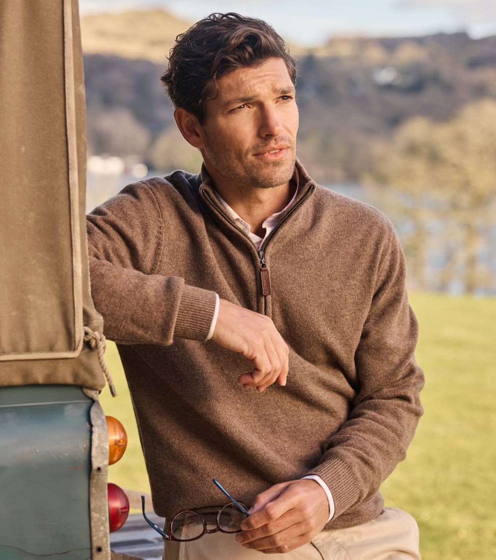 Man in a brown sweatshirt standing next to a vehicle with a scenic background