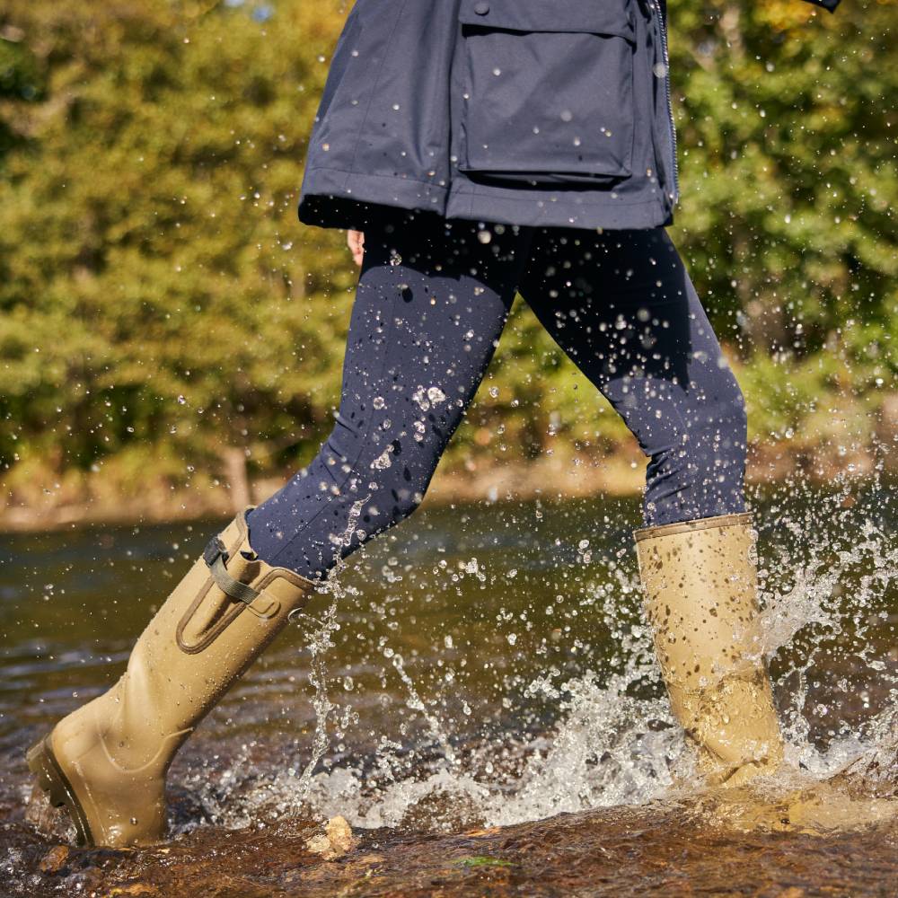 Person wearing green rubber boots splashing in water with a blurred natural background