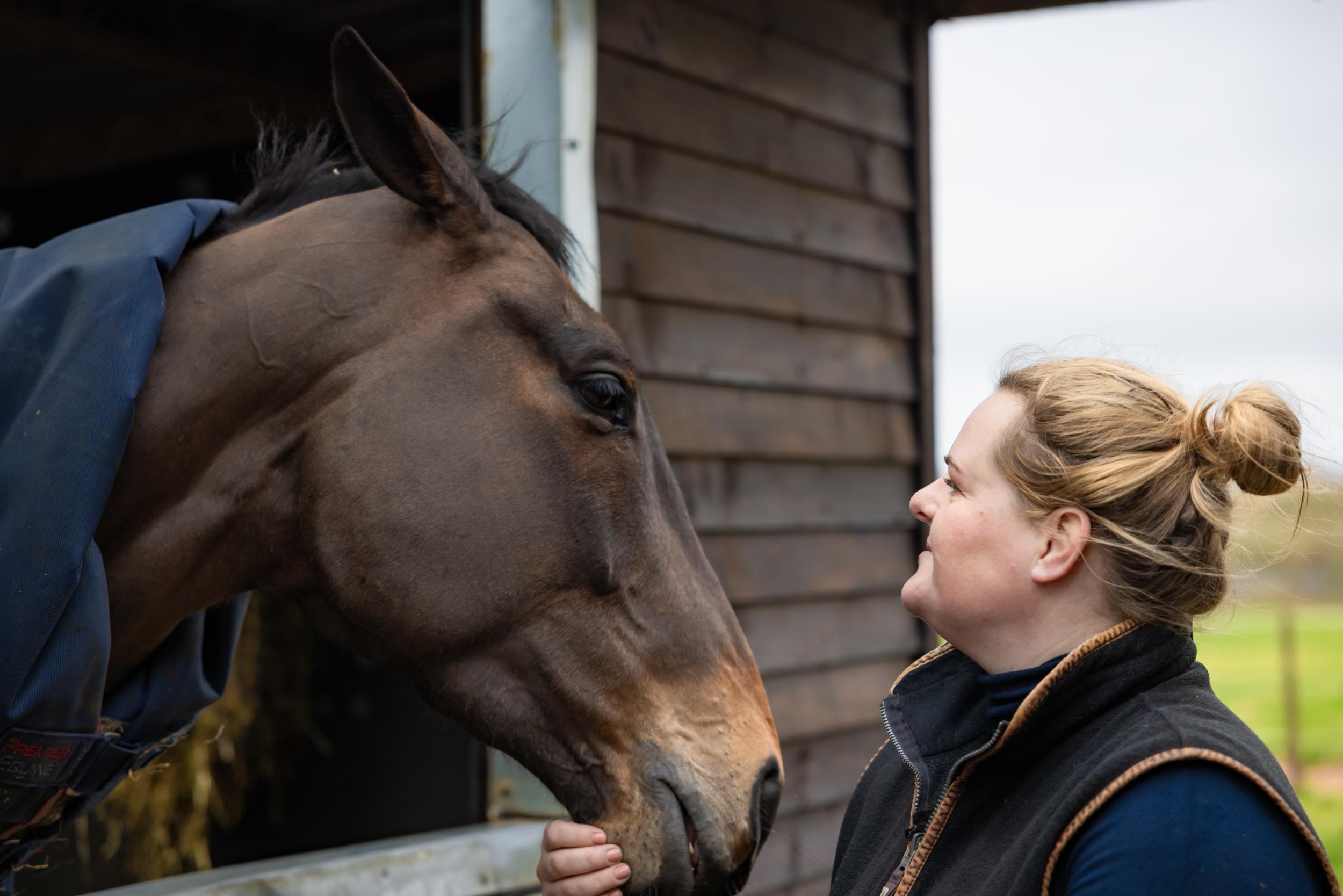 A lady is looking up at her horse over a stable door and holding their chin.
