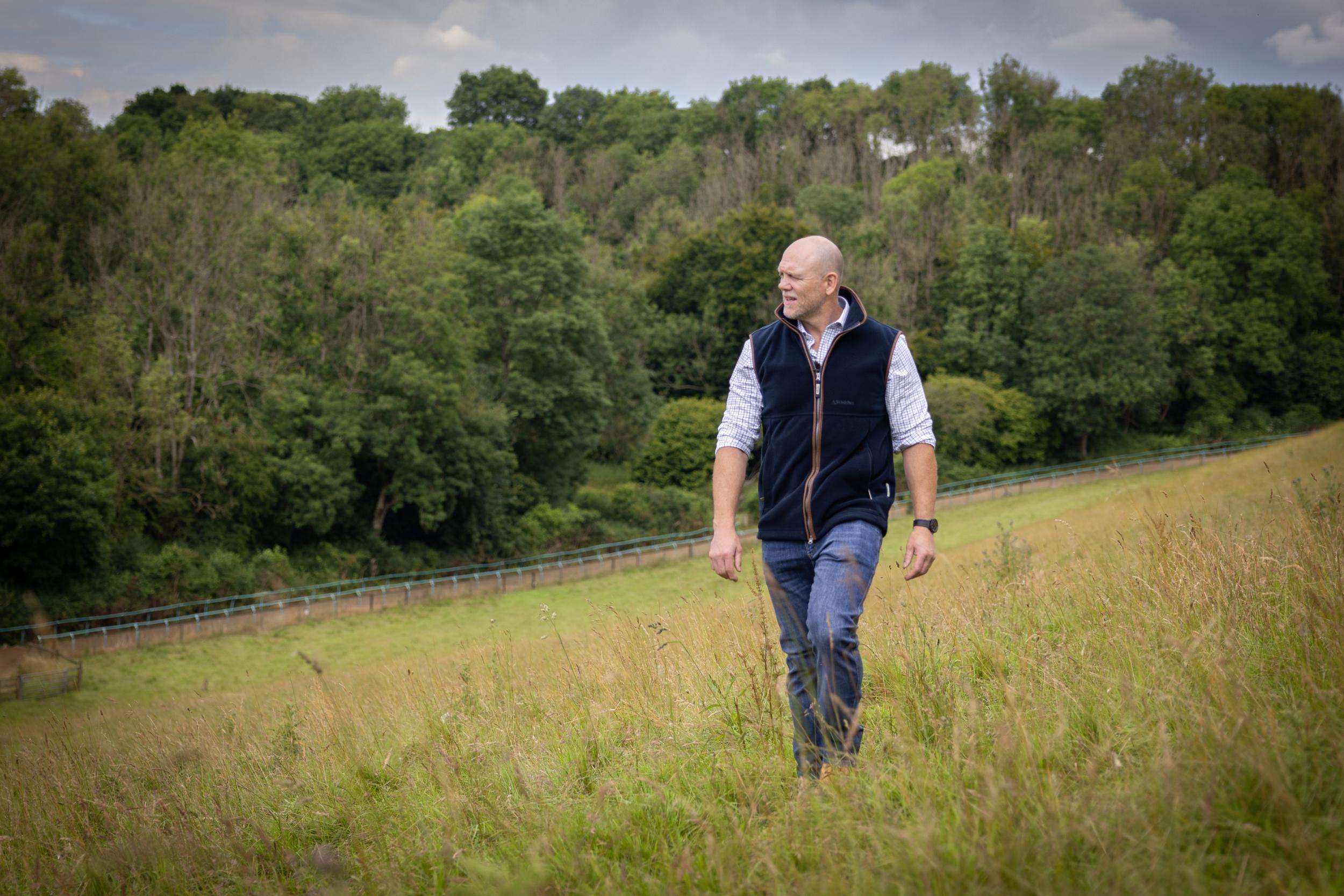 A man walking in open field wearing a navy gilet, checked shirt and jeans.