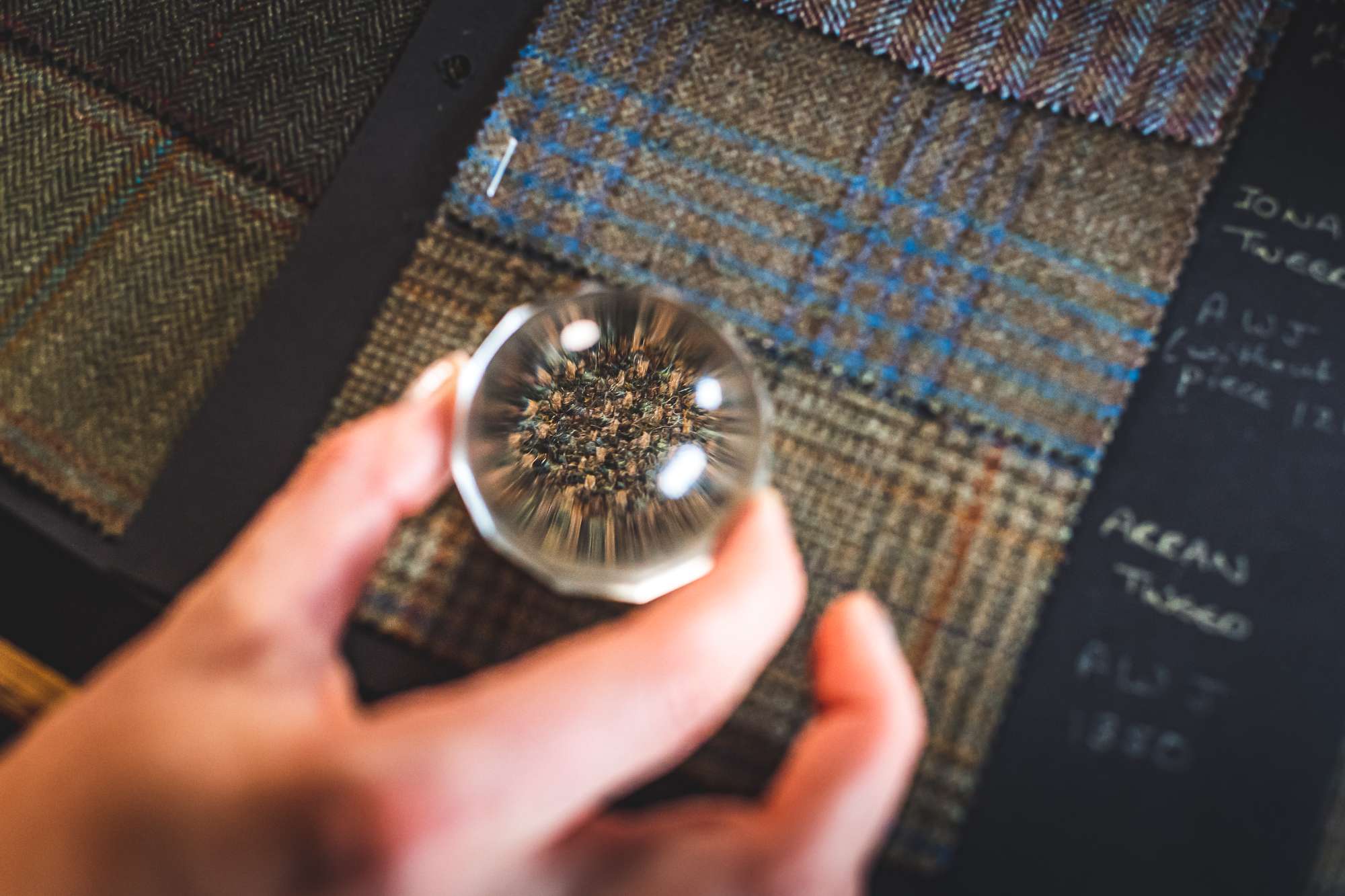 Close up of tweed swatches with a person holding a magnifying glass.