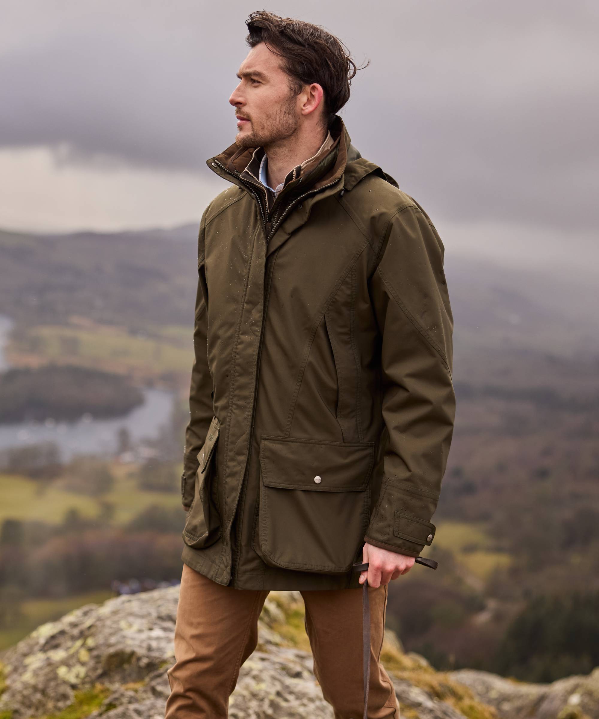 Man wearing a green jacket standing on a rocky outcrop with a scenic background
