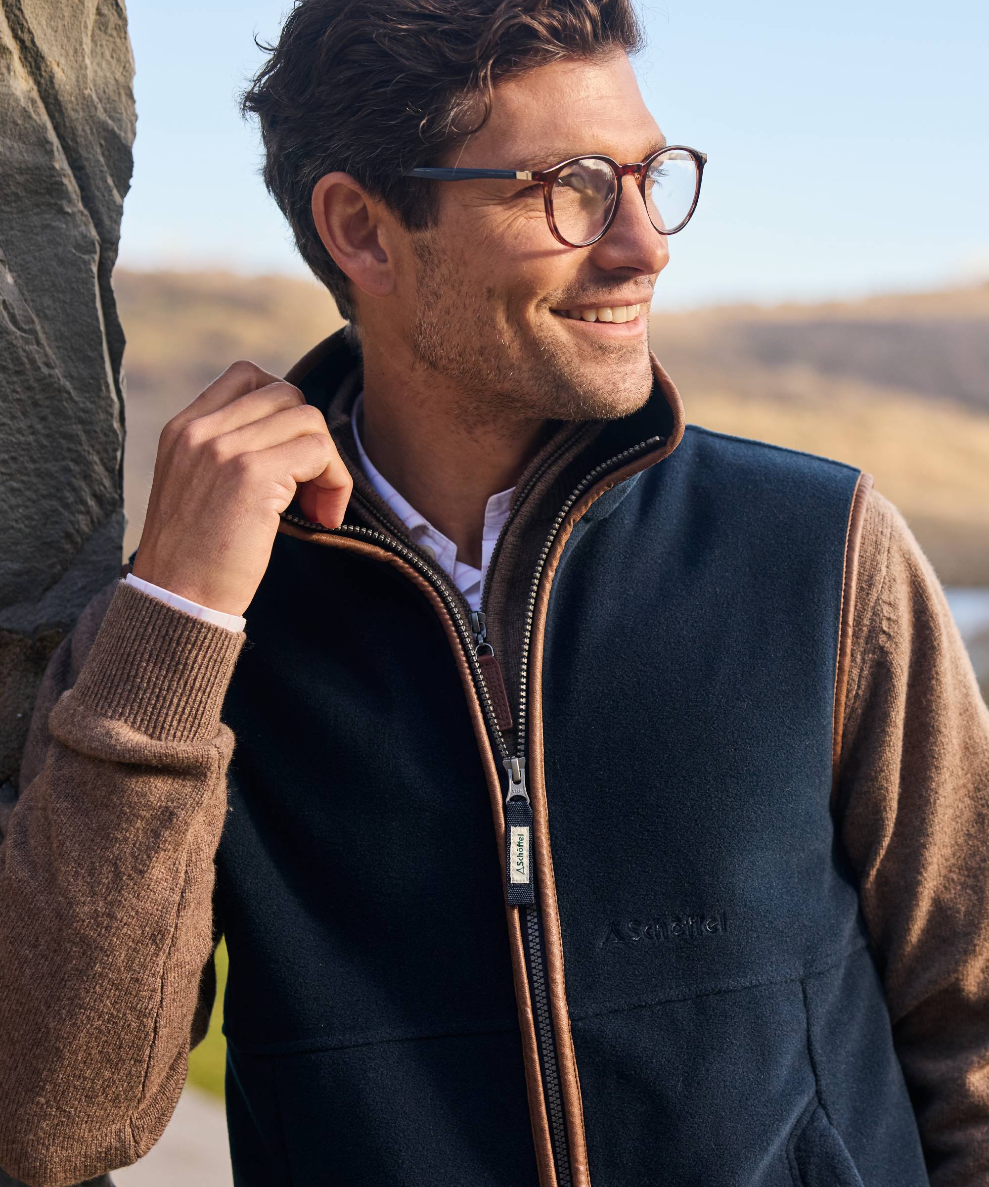 Man wearing a navy gilet over a brown jumper with a blurred outdoor background