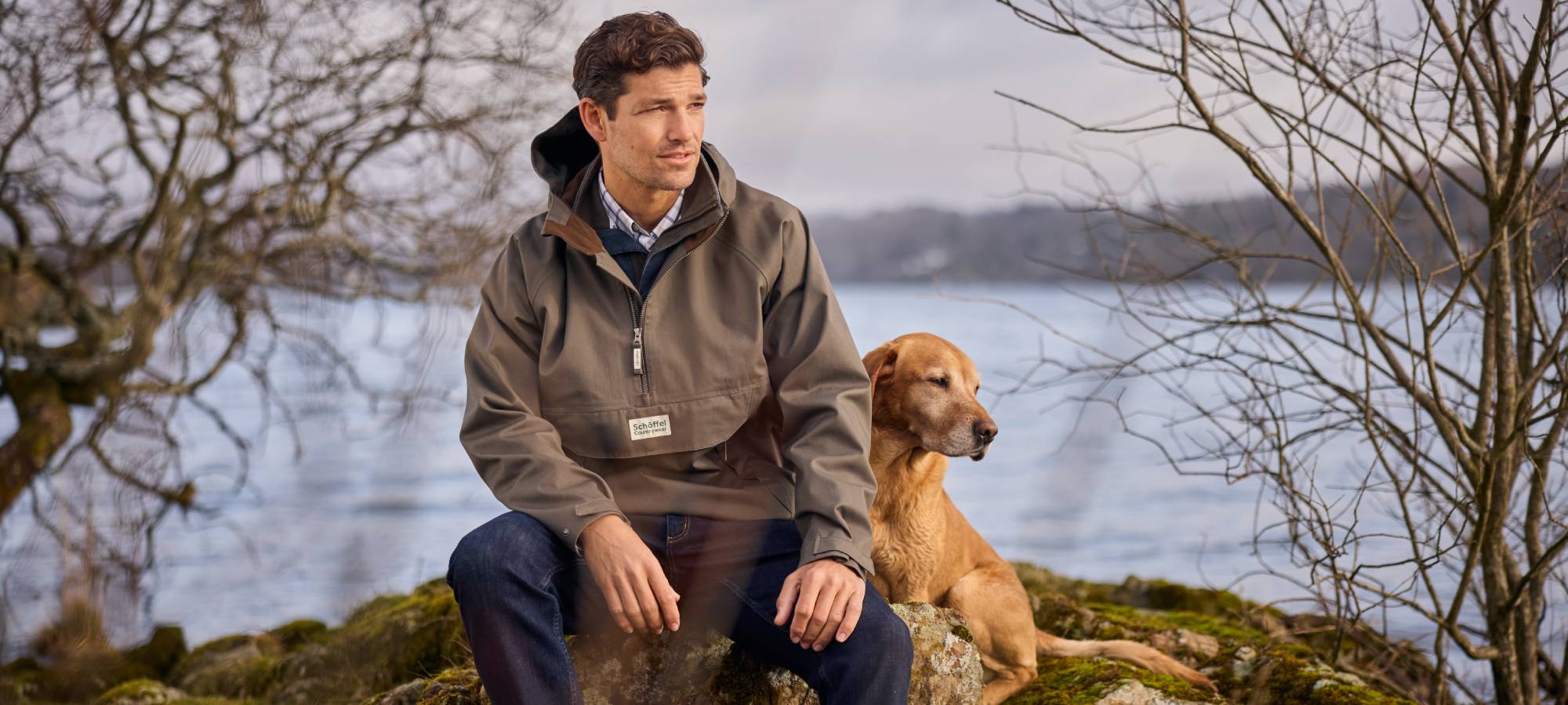 Man sitting on a rock with a dog by a lake