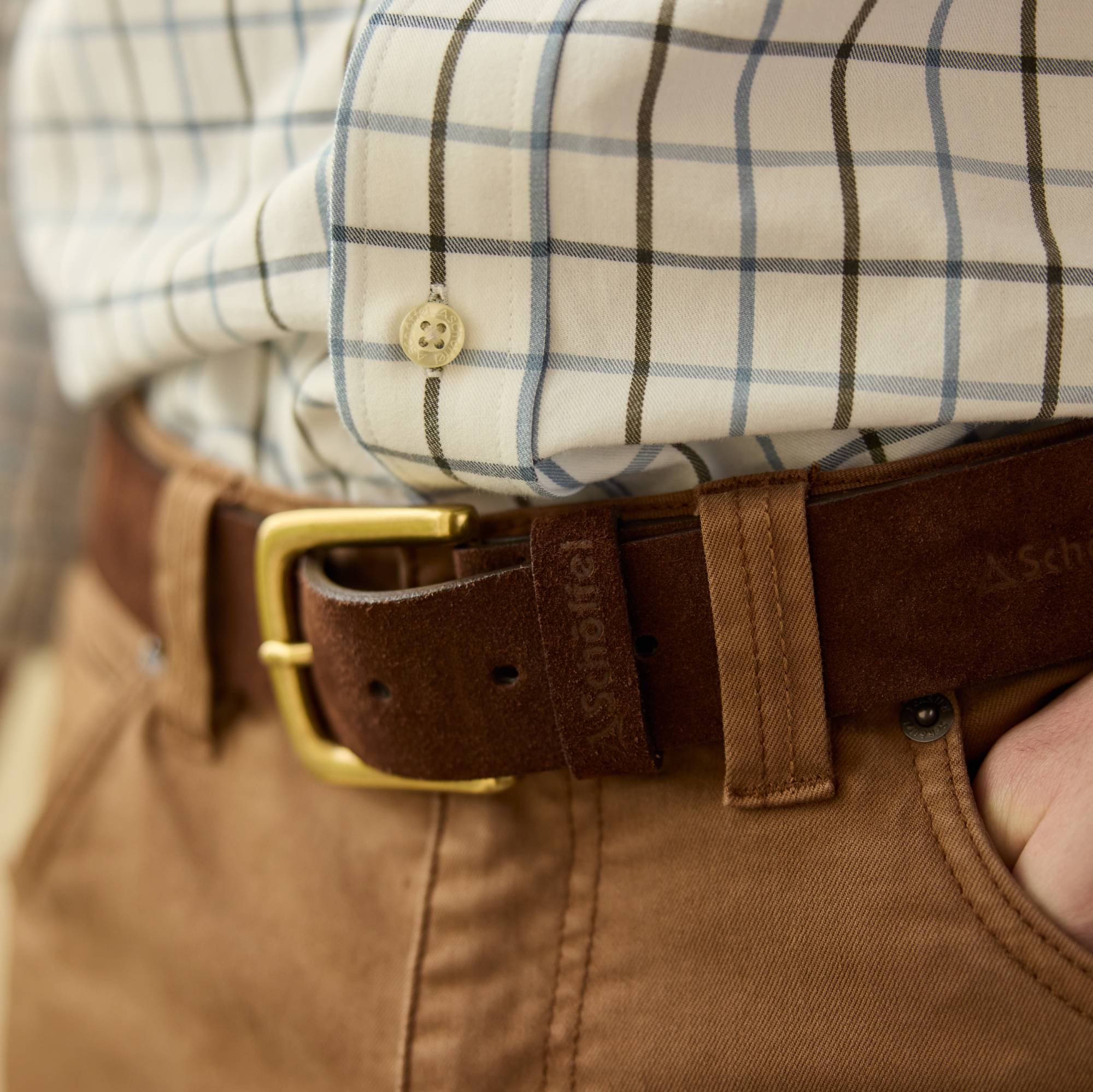 Close-up of a person wearing a checked shirt, brown chinos, and a brown belt with a gold buckle.
