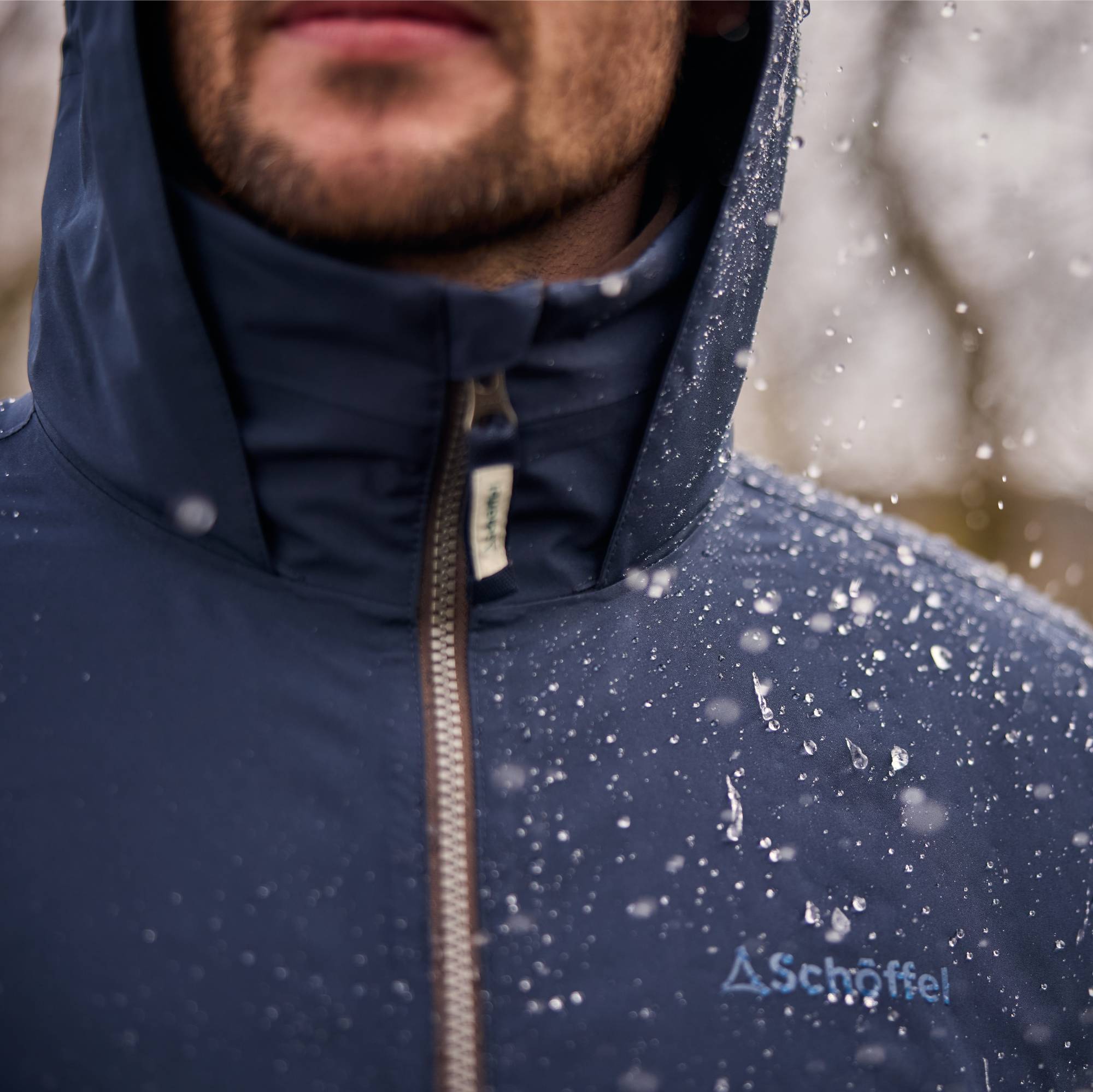 Person wearing a navy blue jacket with a brand logo, standing in a rainy environment.