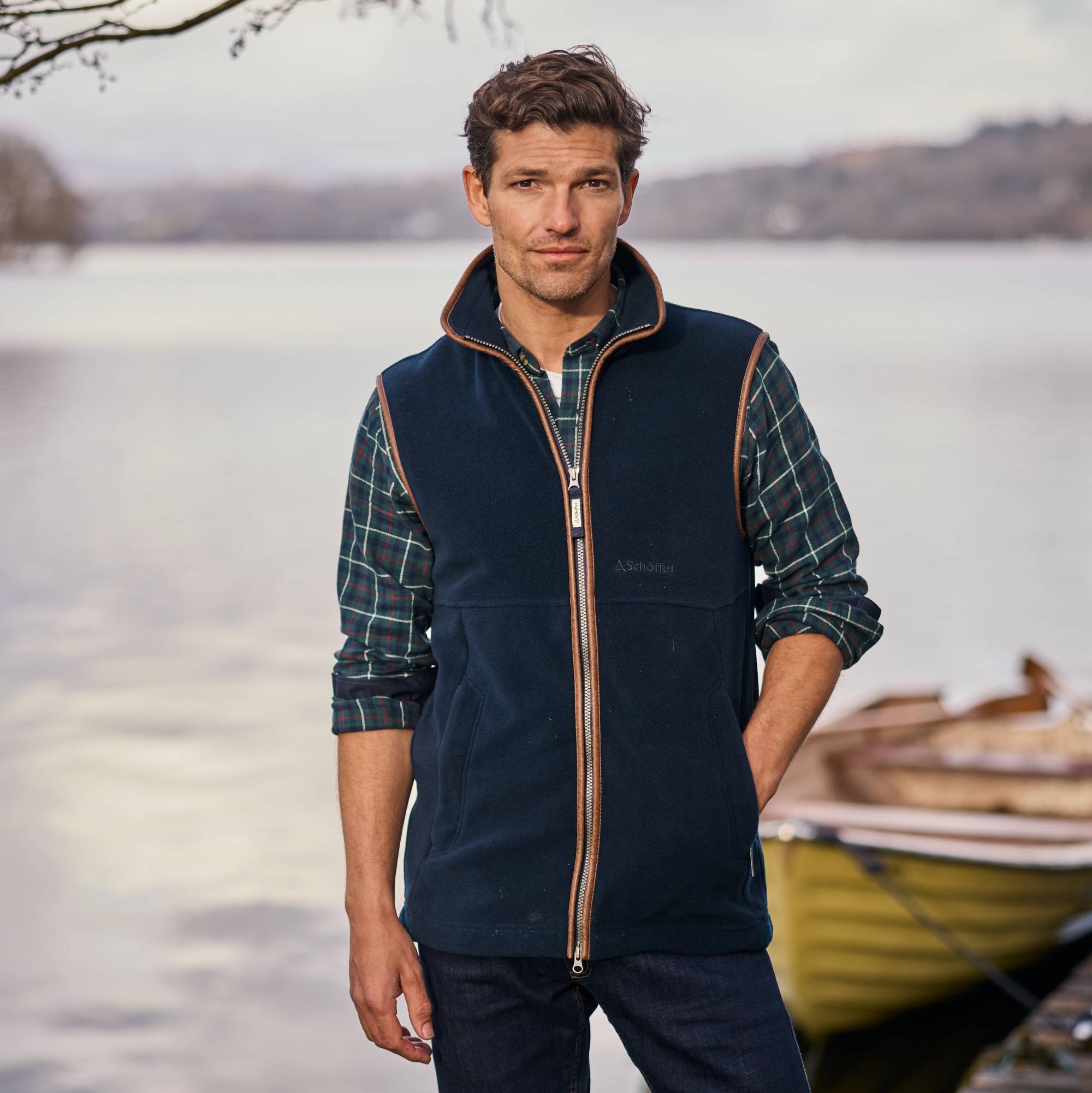 Man wearing a navy fleece gilet by a lake with a boat in the background