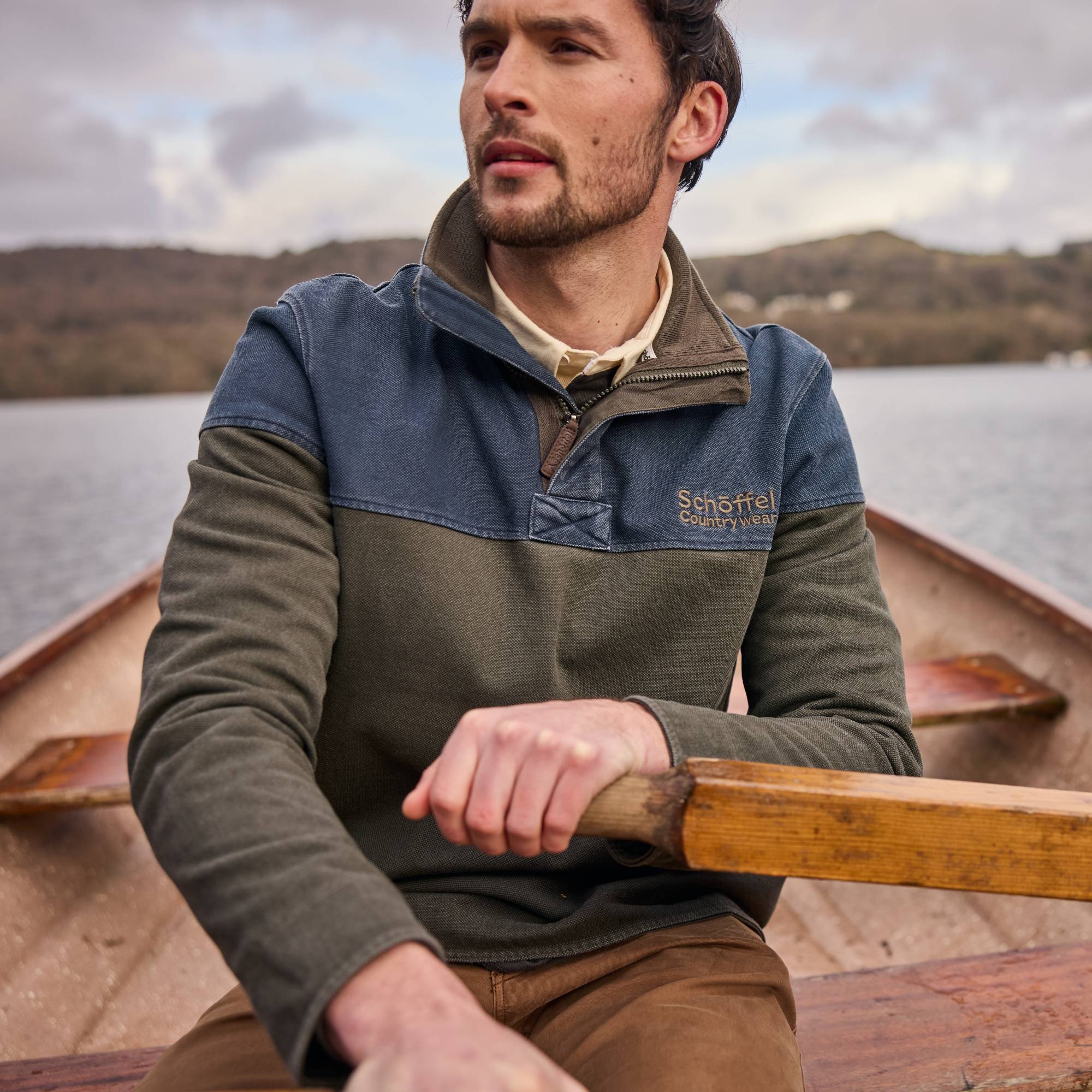 Man rowing a boat wearing a two-tone sweatshirt with a brand logo.