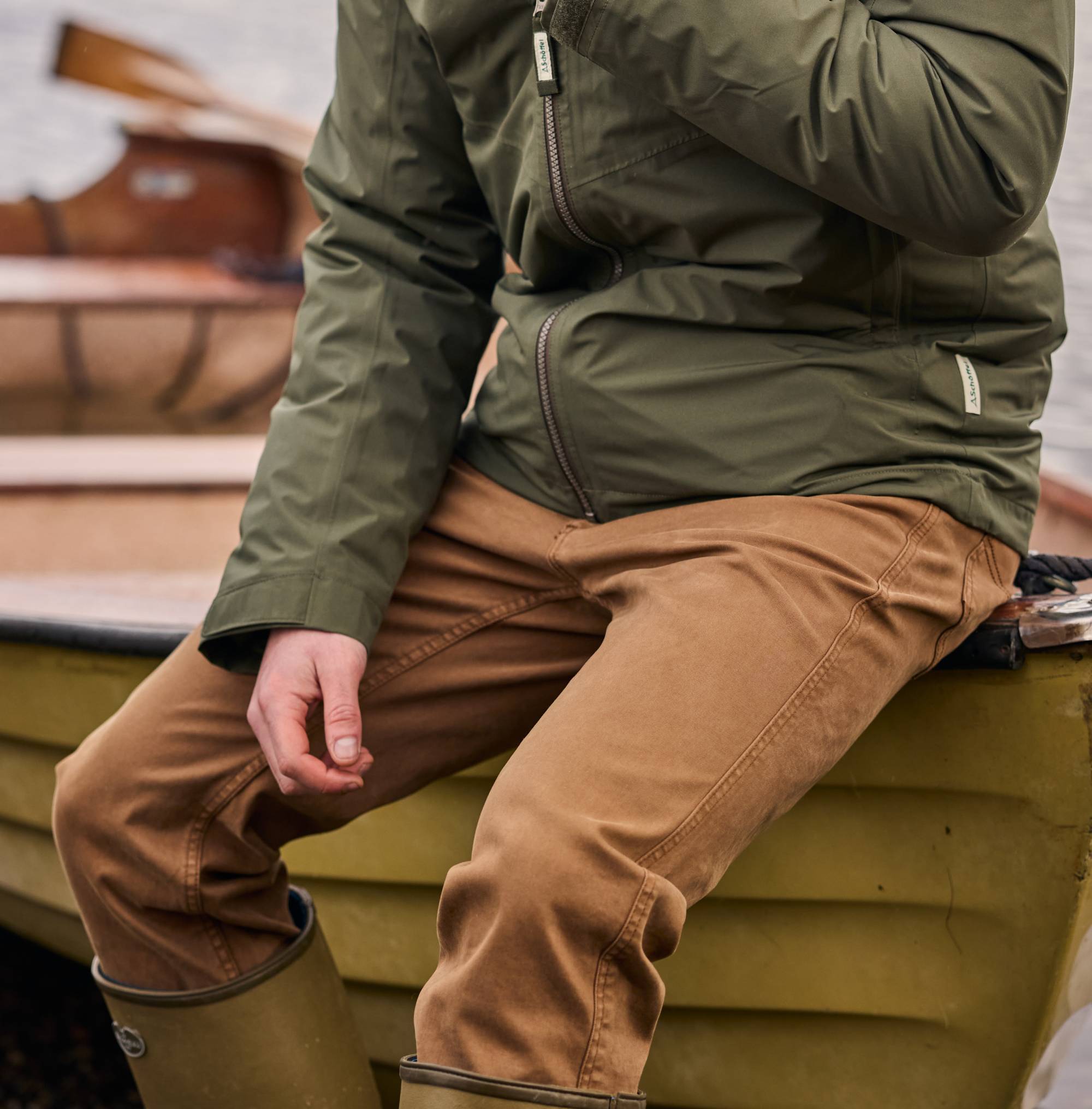 Person wearing a green jacket and brown trousers sitting on a boat.