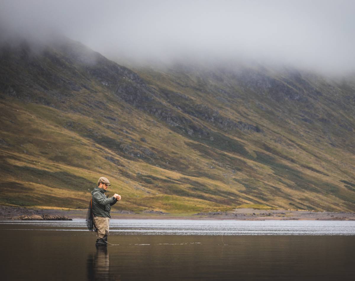 A man fly fishing in a lake surrounded by mountains.
