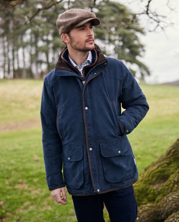 A man wearing a blue jacket and tweed jacket, he is standing in a relaxed pose looking away from the camera.