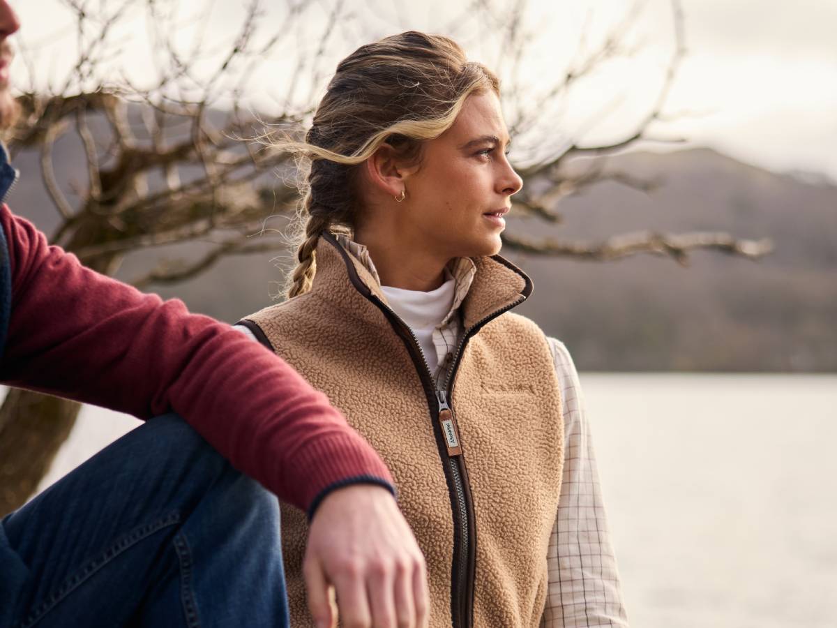 Two people sitting by a lake with trees and water in the background