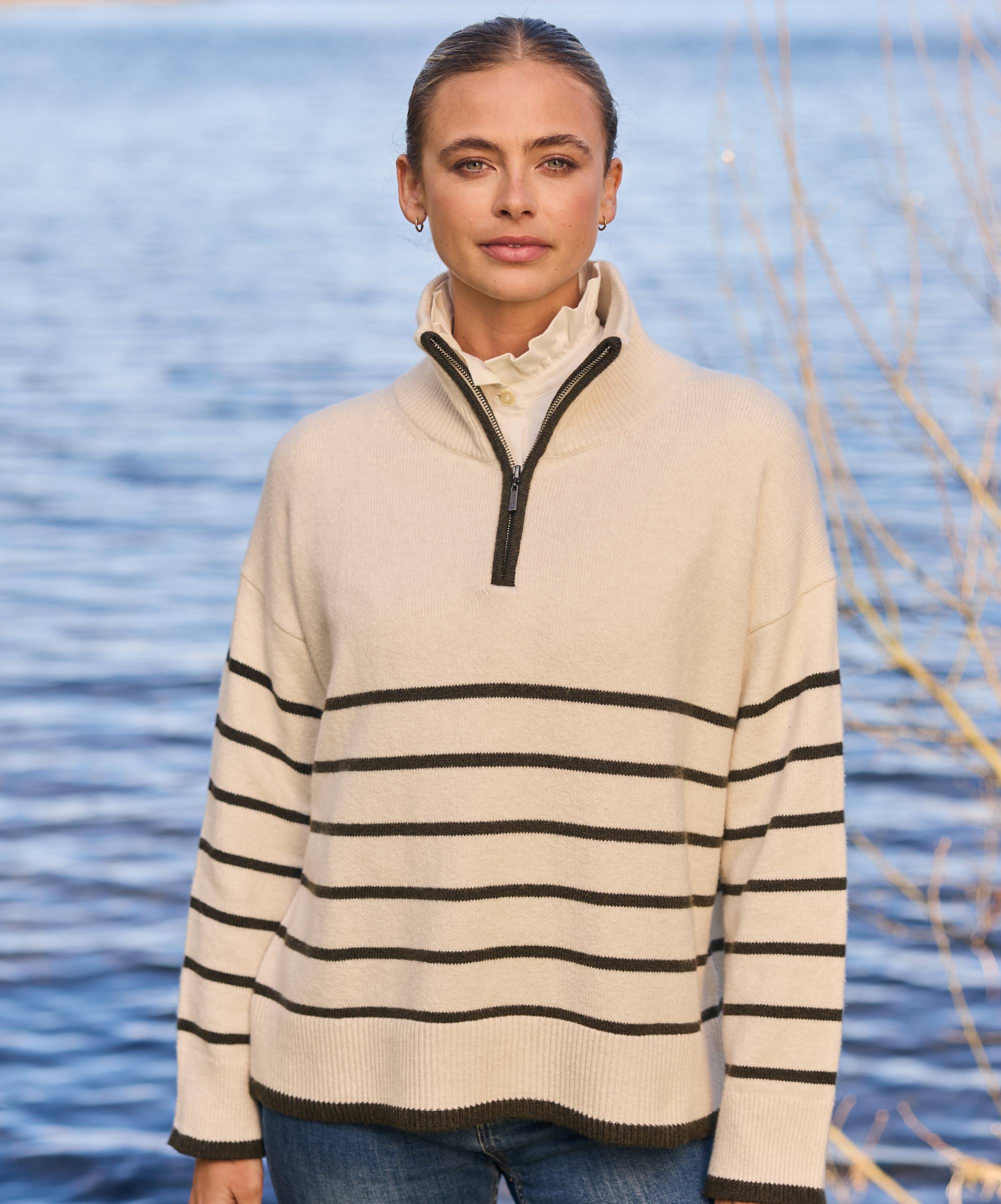 Woman wearing a cream and black striped knitted jumper by a body of water.