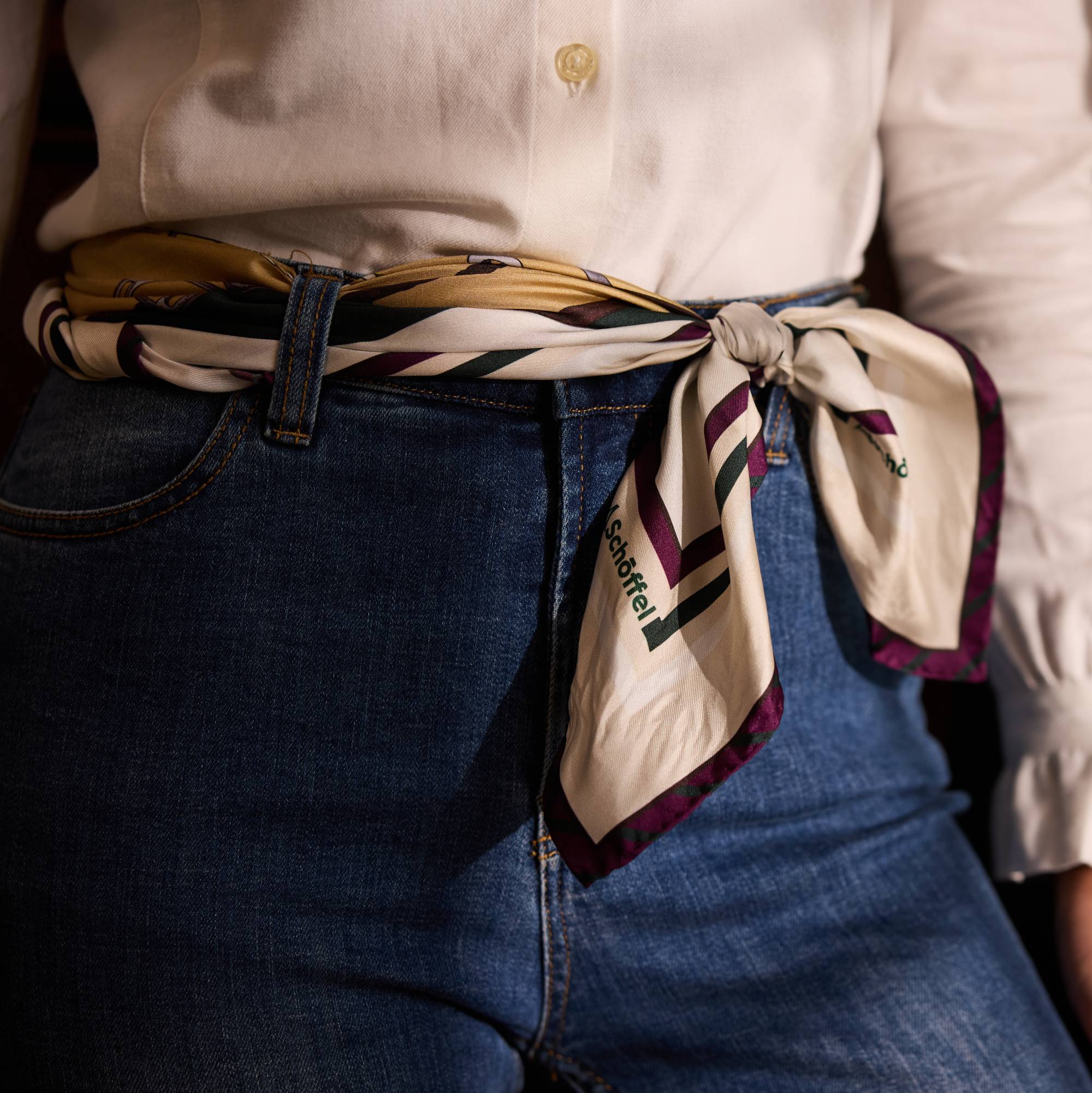 Person wearing a striped scarf tied around their waist over denim jeans and white shirt.