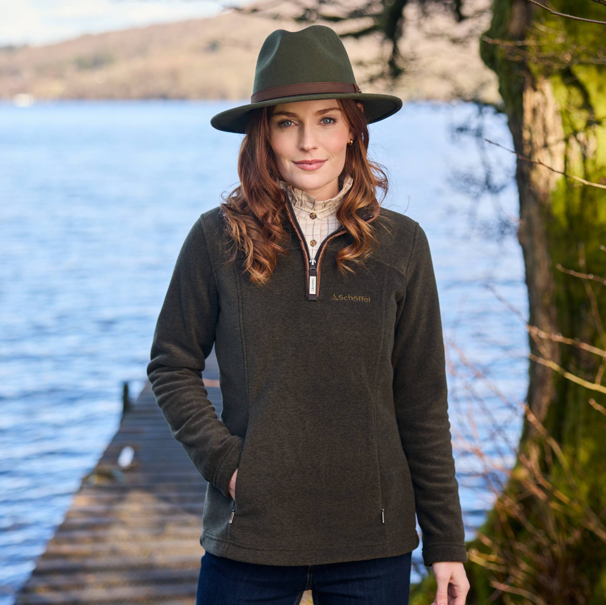 Woman wearing a dark green fleece and hat by a lake