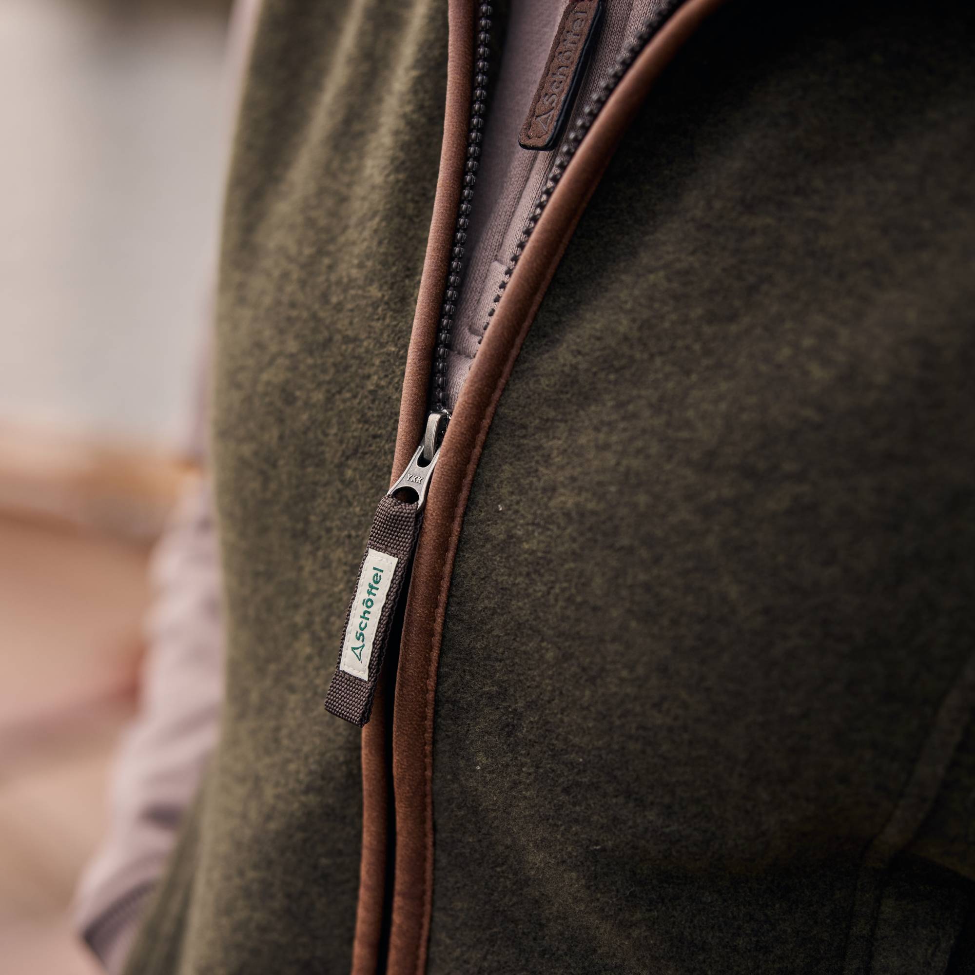 Close-up of a brown zipper on a dark green fleece gilet with a blurred background