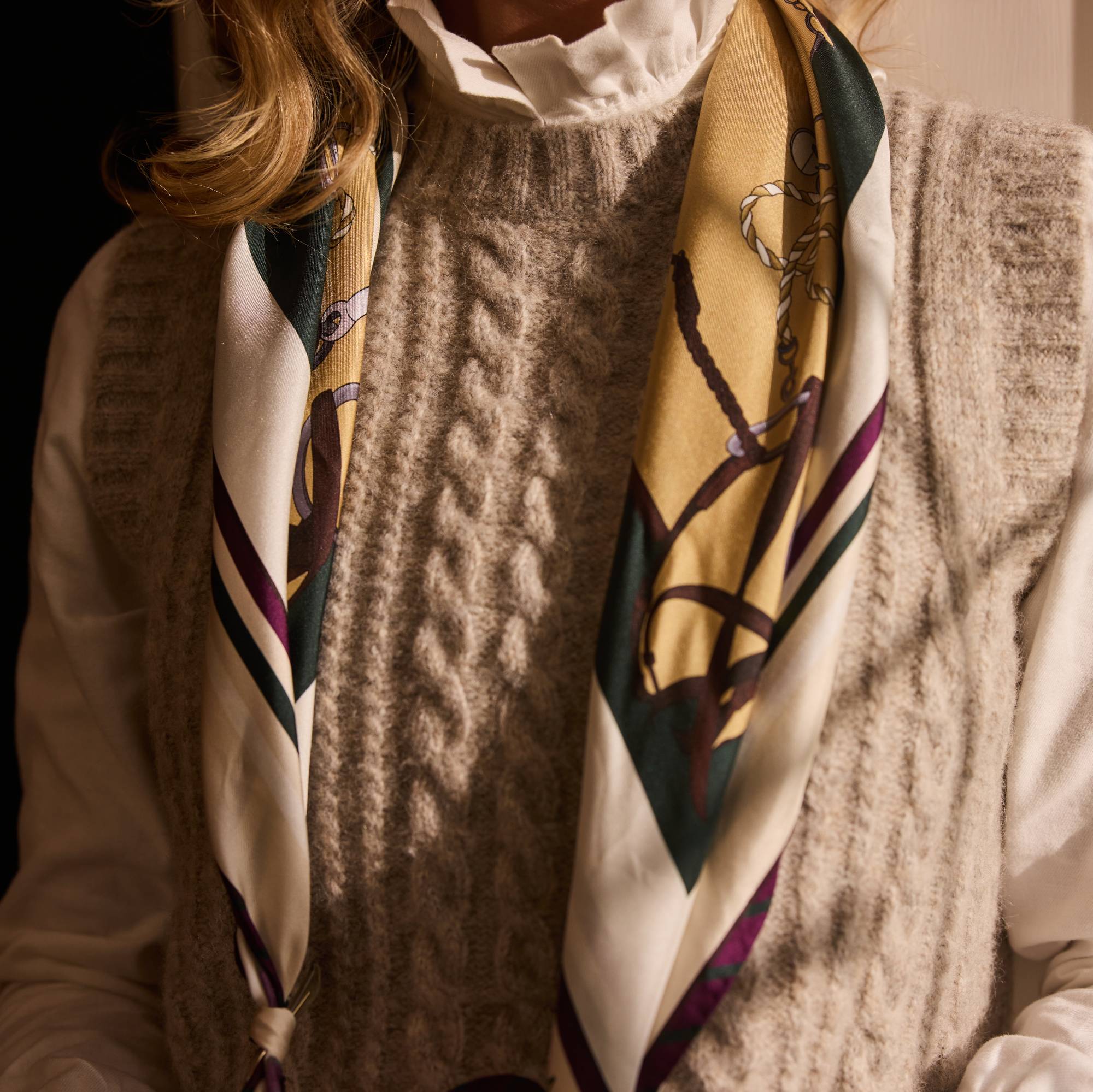 Person wearing a patterned scarf over a textured knitted jumper and white frill collar shirt.