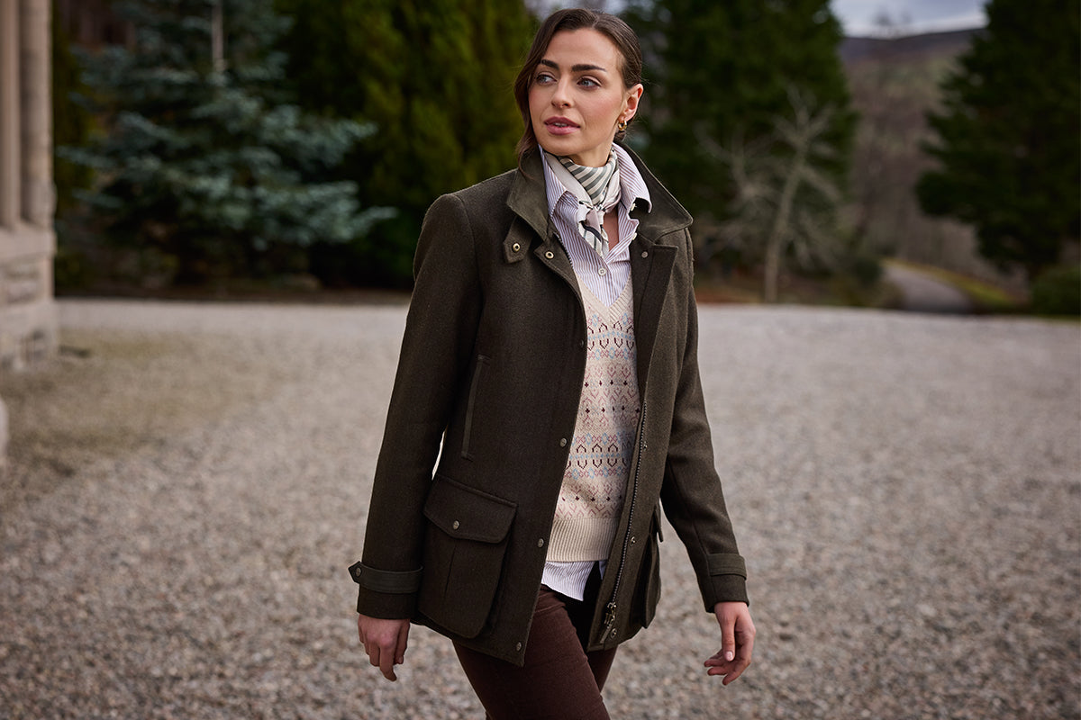 A woman wearing a dark brown mid-length coat over a cream knit sweater and scarf.