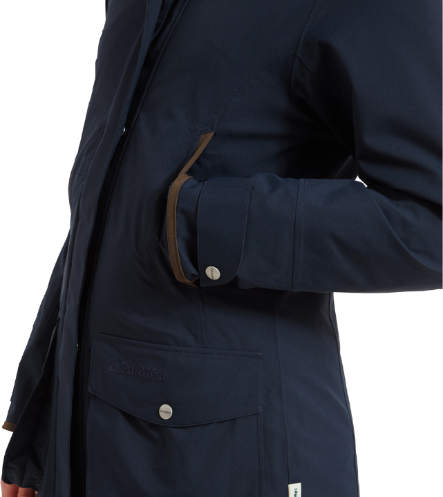 Side-view close-up of a true navy ultralight coat, showing a flap-over hip pocket with a press-stud fastening, a hand-warmer pocket with brown suede-effect trim, and a cuffed sleeve. A small Schöffel logo is embossed near the hem.