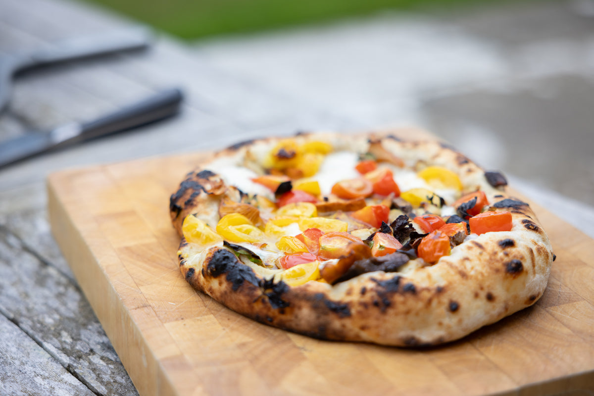 A small round pizza with charred crust,  served on a wooden cutting board.