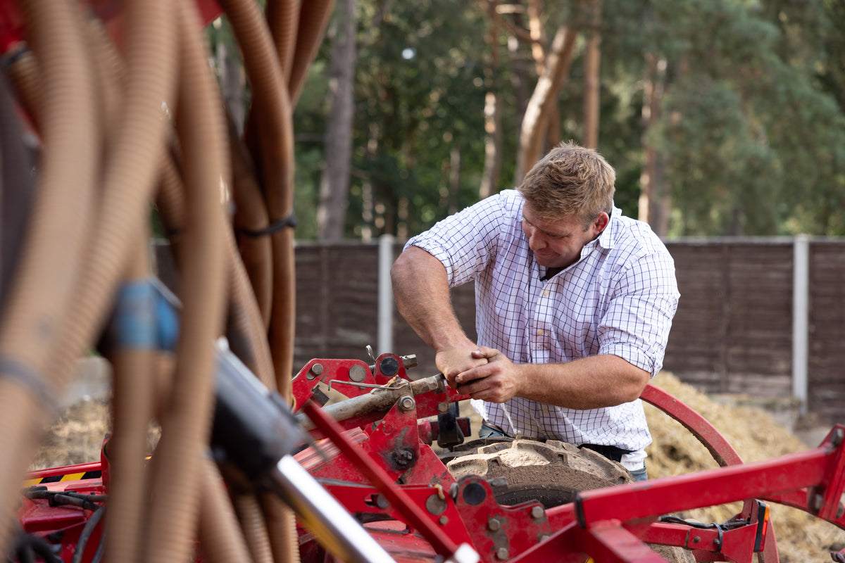 Tom Youngs in a check shirt repairing a broken seed drill in the farmyard