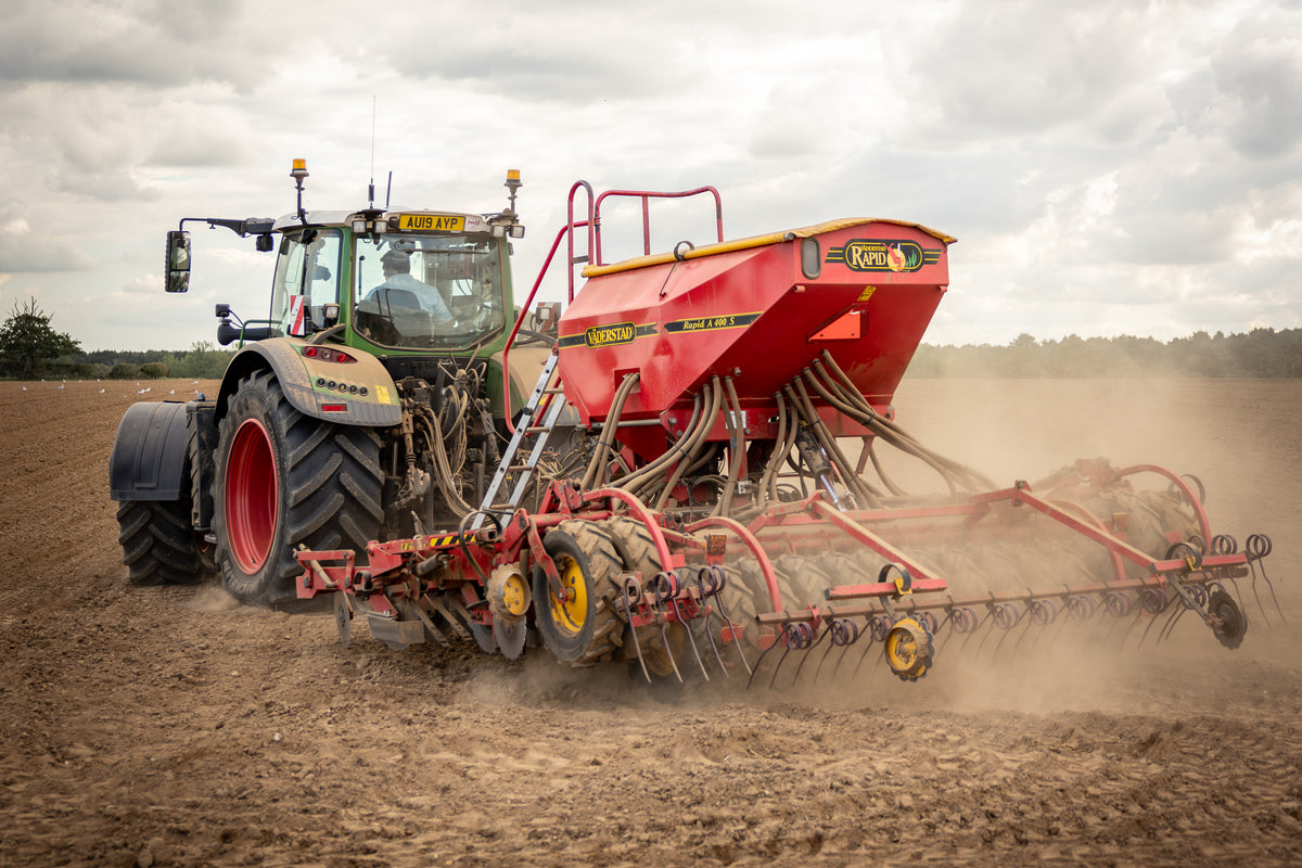 Tractor pulling a red seed drill across a dusty field during autumn drilling on Tom Youngs' farm
