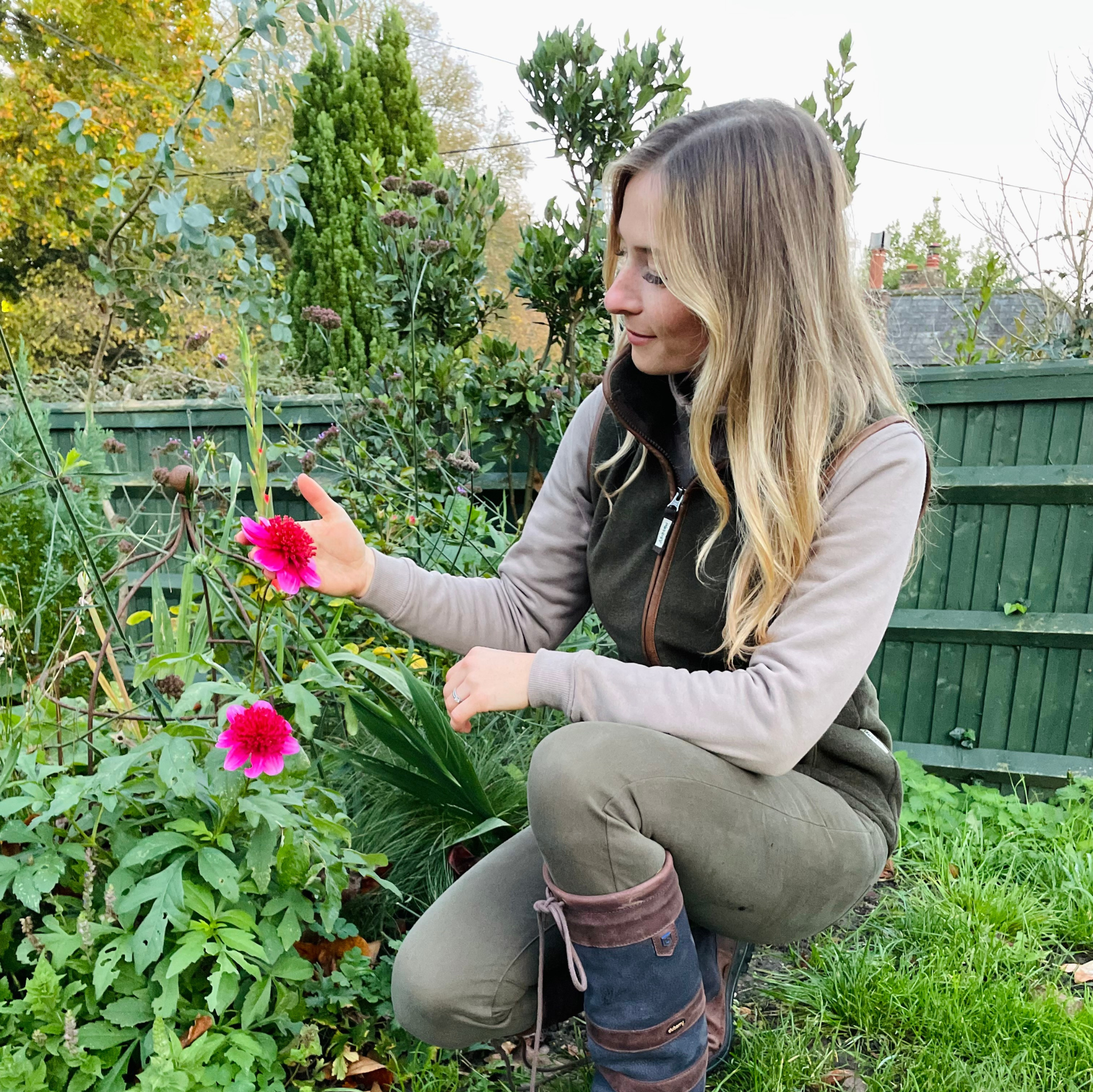 Woman in a garden examining a pink flower