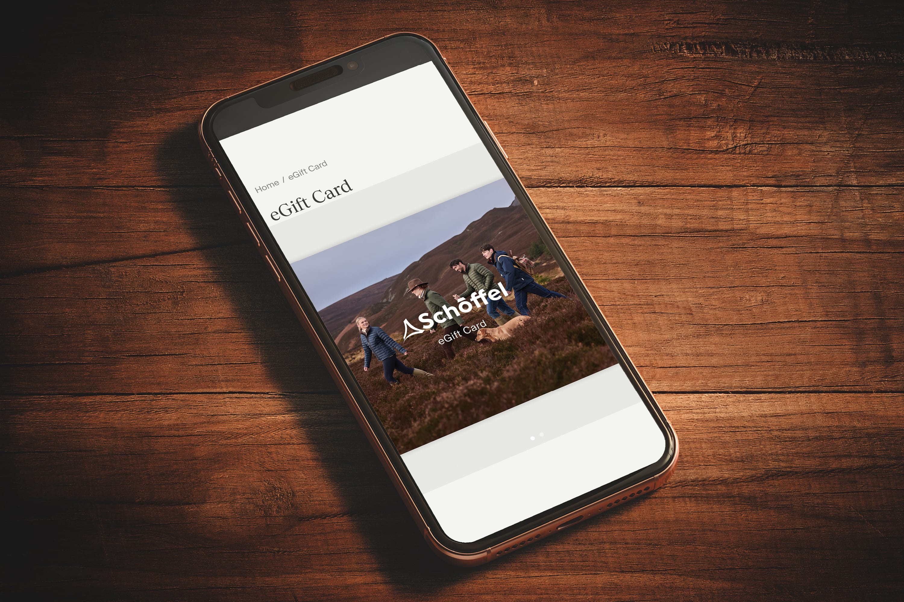 A sleek black smartphone displaying a schöffel egift card interface with hikers in the mountains in eGift card product