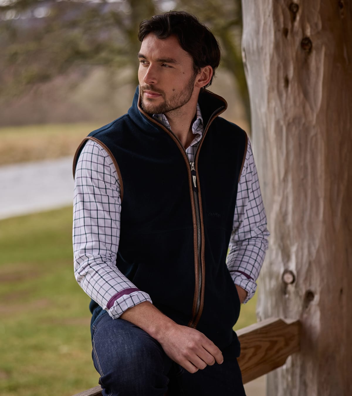 Man wearing navy fleece gilet with tan leather trim over check shirt