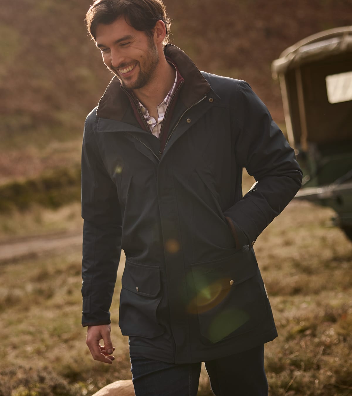 Man wearing navy waterproof jacket with brown corduroy collar walking in golden hour countryside
