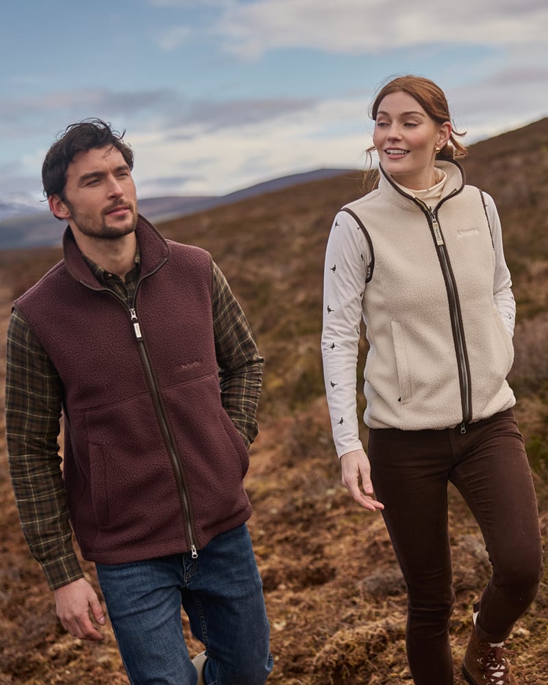 A man and a woman walking outdoors in a hilly, grassy landscape.