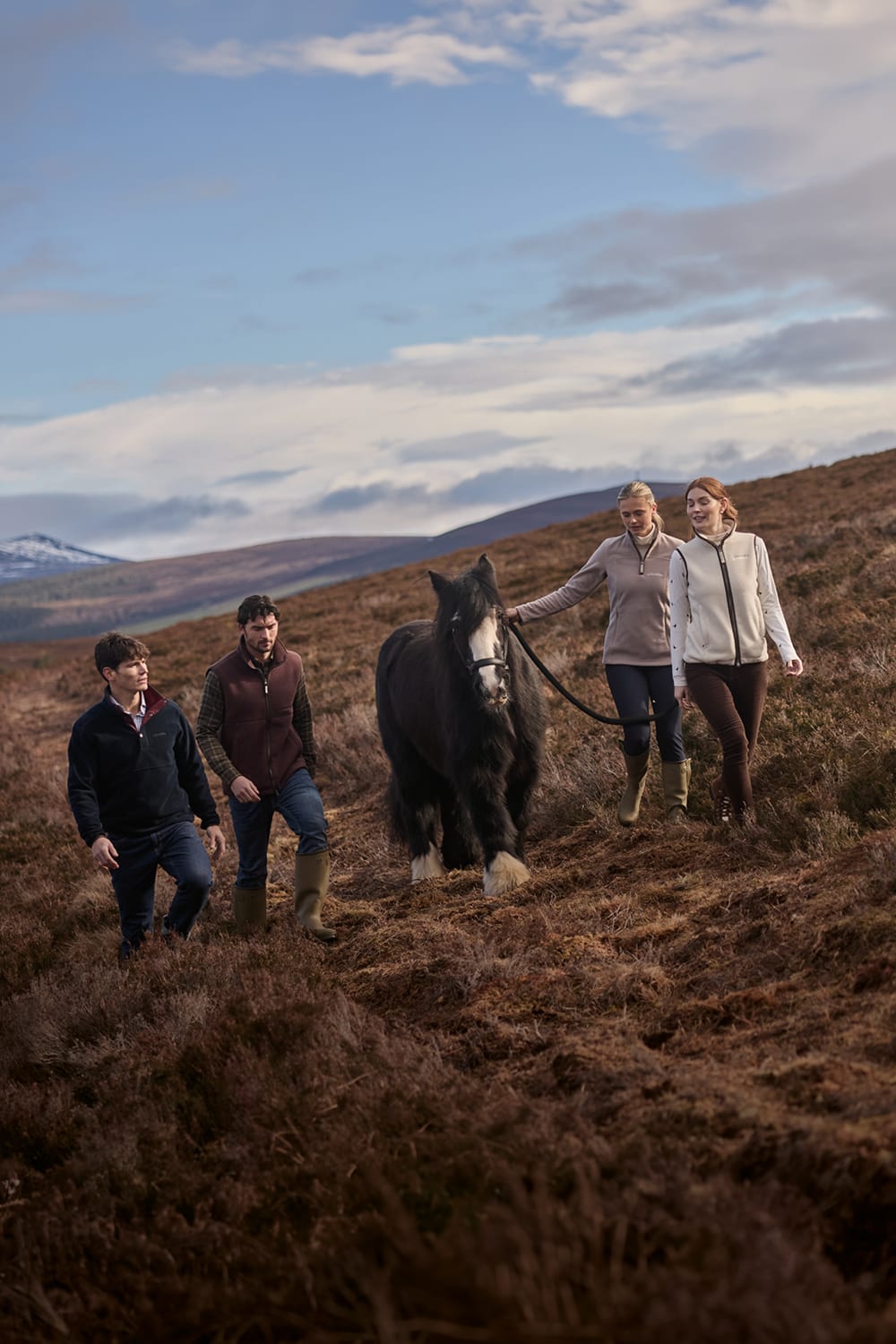 Four people walking across a grassy hillside with a large black horse.