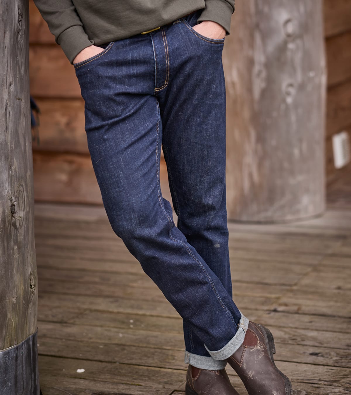 A person wearing blue denim jeans with rolled cuffs, paired with brown boots and an olive green top.