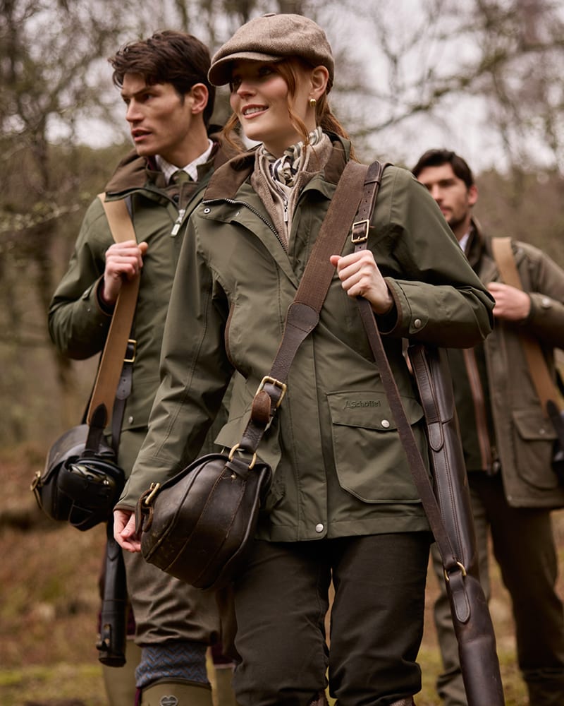Three people outdoors in a wooded setting wearing olive green shooting jackets.