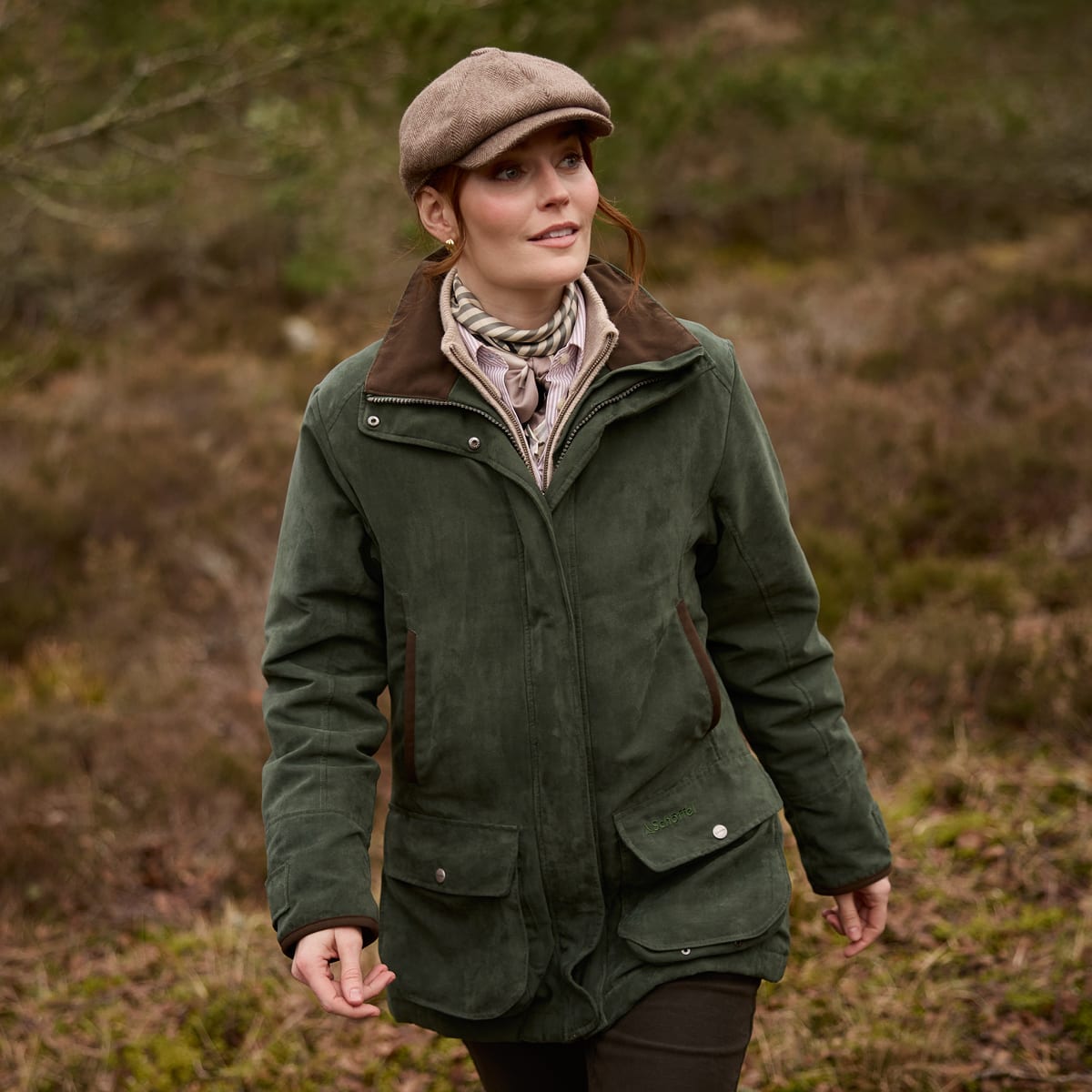 A woman wearing a green jacket with brown corduroy collar, walking outdoors in a grassy environment.