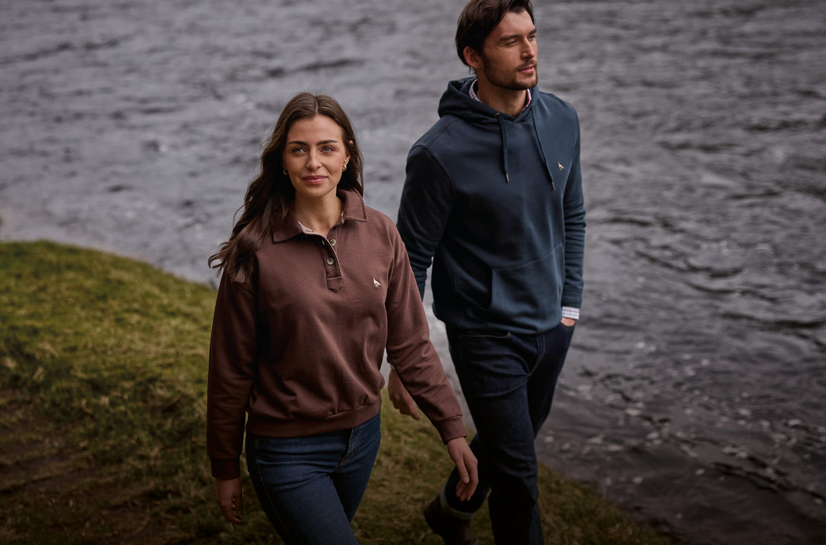 A man and a woman walking outdoors wearing blue and brown sweaters
